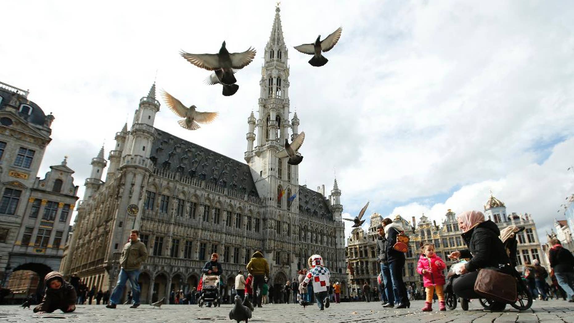 Pigeons take flight as tourists feed them in the Grand Place in Brussels, Monday, March, 28, 2016. The Belgian health minister says four of those wounded in the suicide bombings last week have died in the hospital.(AP Photo/Alastair Grant)