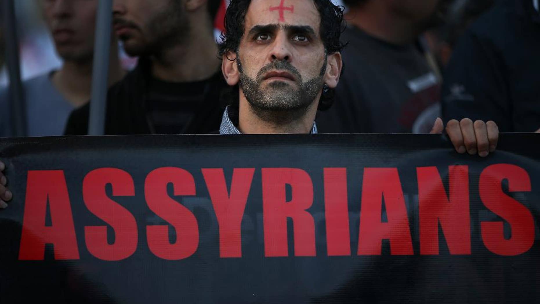 FILE - In this Saturday, Feb. 28, 2015 file photo, an Assyrian man with a red cross painted on his forehead holds a banner as he walks during a protest of several hundred people in solidarity with Christians abducted in Syria and Iraq, in downtown Beirut, Lebanon. Activists said on Saturday, March. 7, 2015, that Islamic State militants have attacked a string of predominantly Christian villages in northeastern Syria, touching off heavy clashes with Kurdish militiamen and their local allies. (AP Photo/Hussein Malla, File)