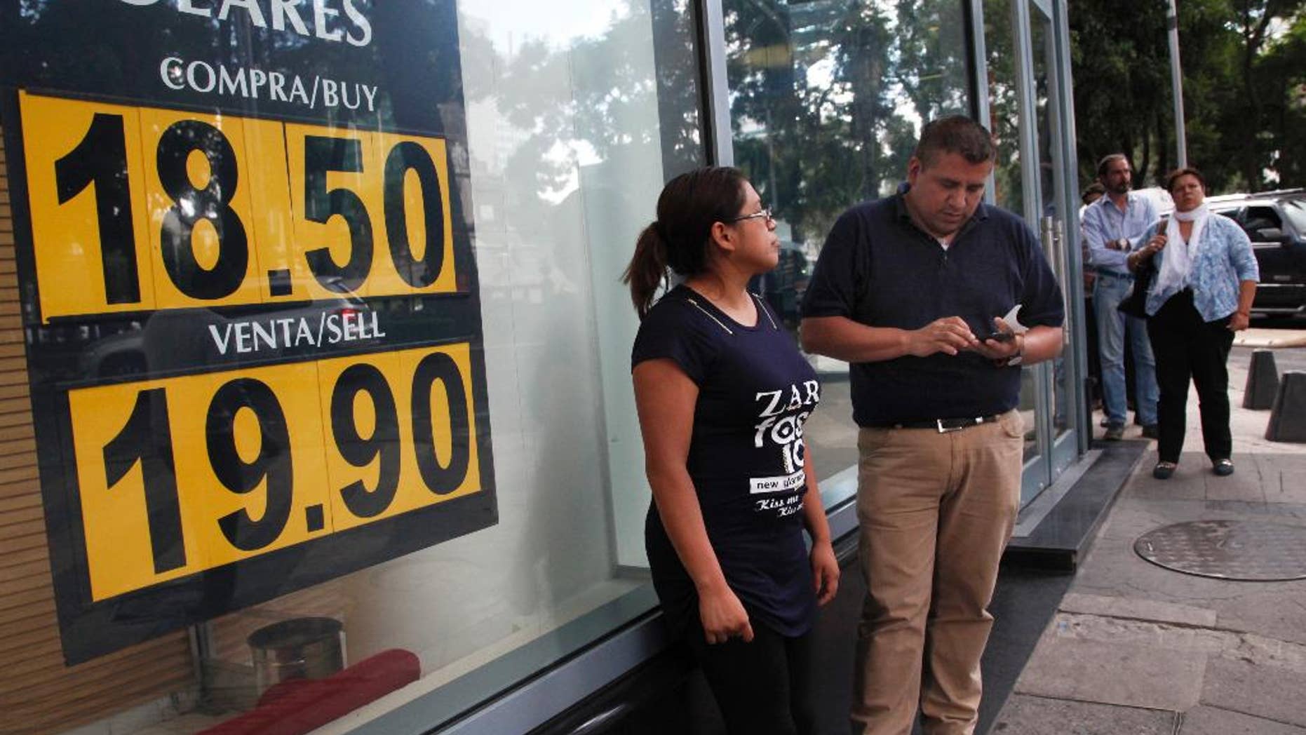 FILE - In this Sept. 19, 2016 file photo, people stand outside an exchange house advertising the sale of U.S. dollars at the rate of 19.90 Mexican pesos per dollar in Mexico City. U.S. election day cannot come soon enough for the Mexican peso, especially if Hillary Clinton is the winner. The currency has been pummeled in 2016, losing close to 10 percent of its value against the U.S. dollar, and briefly breaking the psychological barrier of 20 pesos per dollar. Its few bright spots have come after Clinton’s debate performances against Donald Trump. (Photo AP Photo/Marco Ugarte, File)