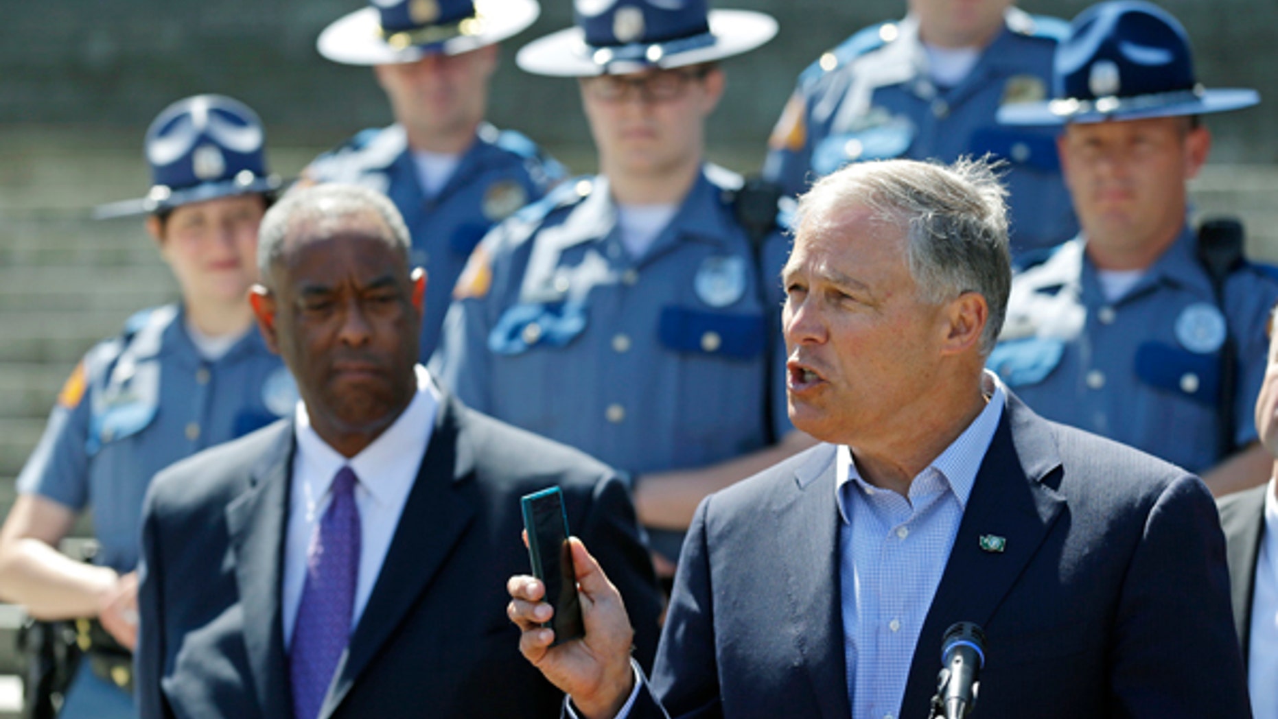 Washington Gov. Jay Inslee, right, holds a cell phone as he speaks during a press event at the Capitol in Olympia, Wash., to raise awareness of Washington state's new law prohibiting the use of nearly all phones and mobile devices while driving.