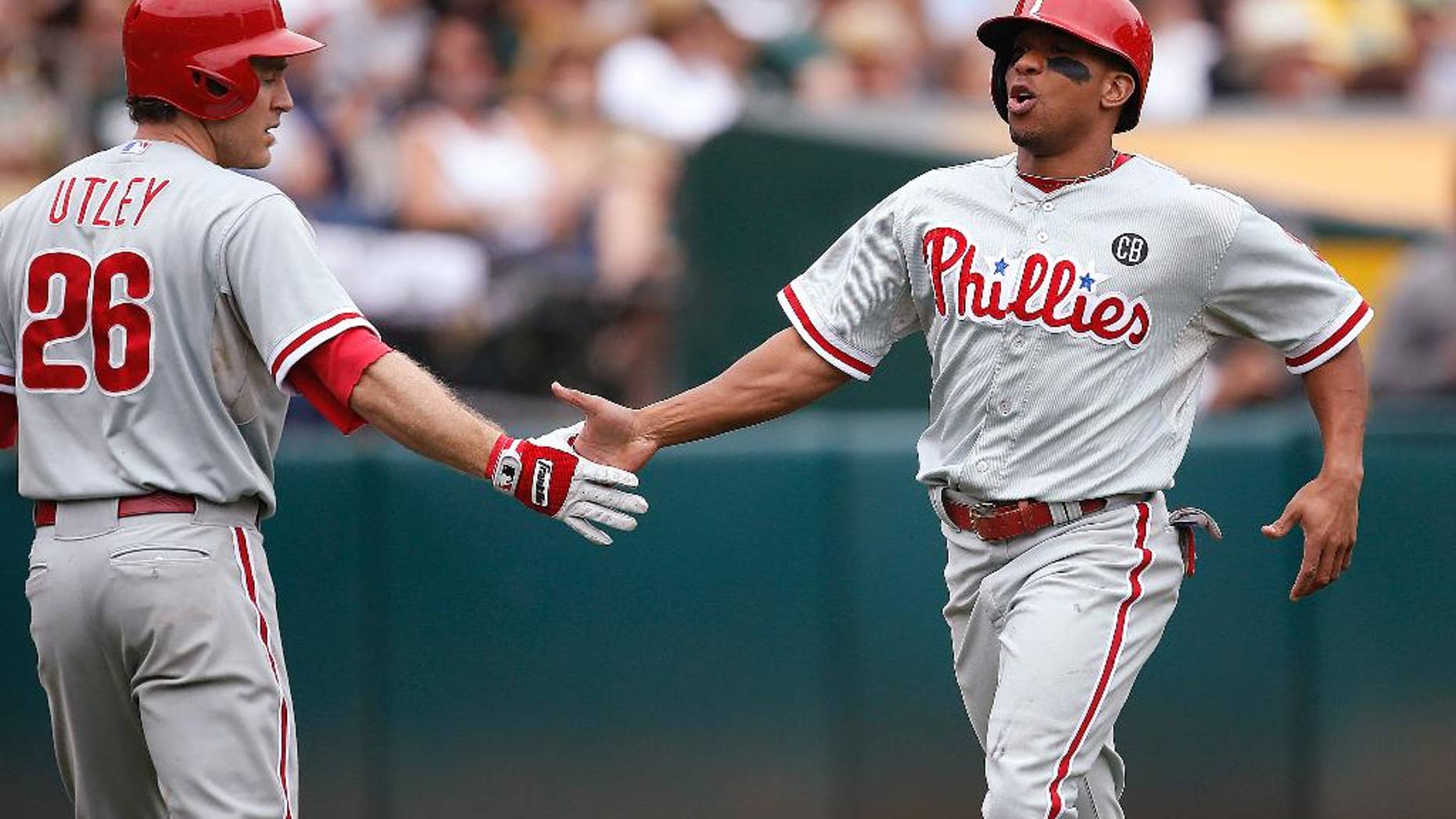 Philadelphia Phillies' Ben Revere, right, is congratulated by Chase Utley after scoring on a hit by Carlos Ruiz against the Oakland Athletics in the fourth inning of a baseball game Sunday, Sept. 21, 2014, in Oakland, Calif. (AP Photo/Tony Avelar)