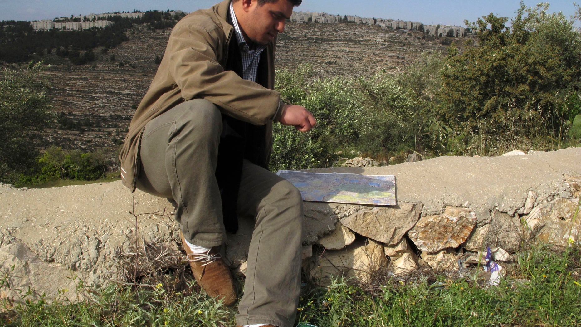 In this Friday, April 19, 2013 photo, George Abu Eid, 22, sits with the map of the area near the village of Beit Jala in the Cremisan Valley, West Bank. Abu Eid's family land is threatened with expropriation to build Israel’s separation barrier. Palestinian residents of this Christian village are hoping the new pope can succeed where others have failed as they press the Israeli government to drop plans to build a stretch of its West Bank separation barrier through their ancestral lands. (AP Photo/Diaa Hadid)