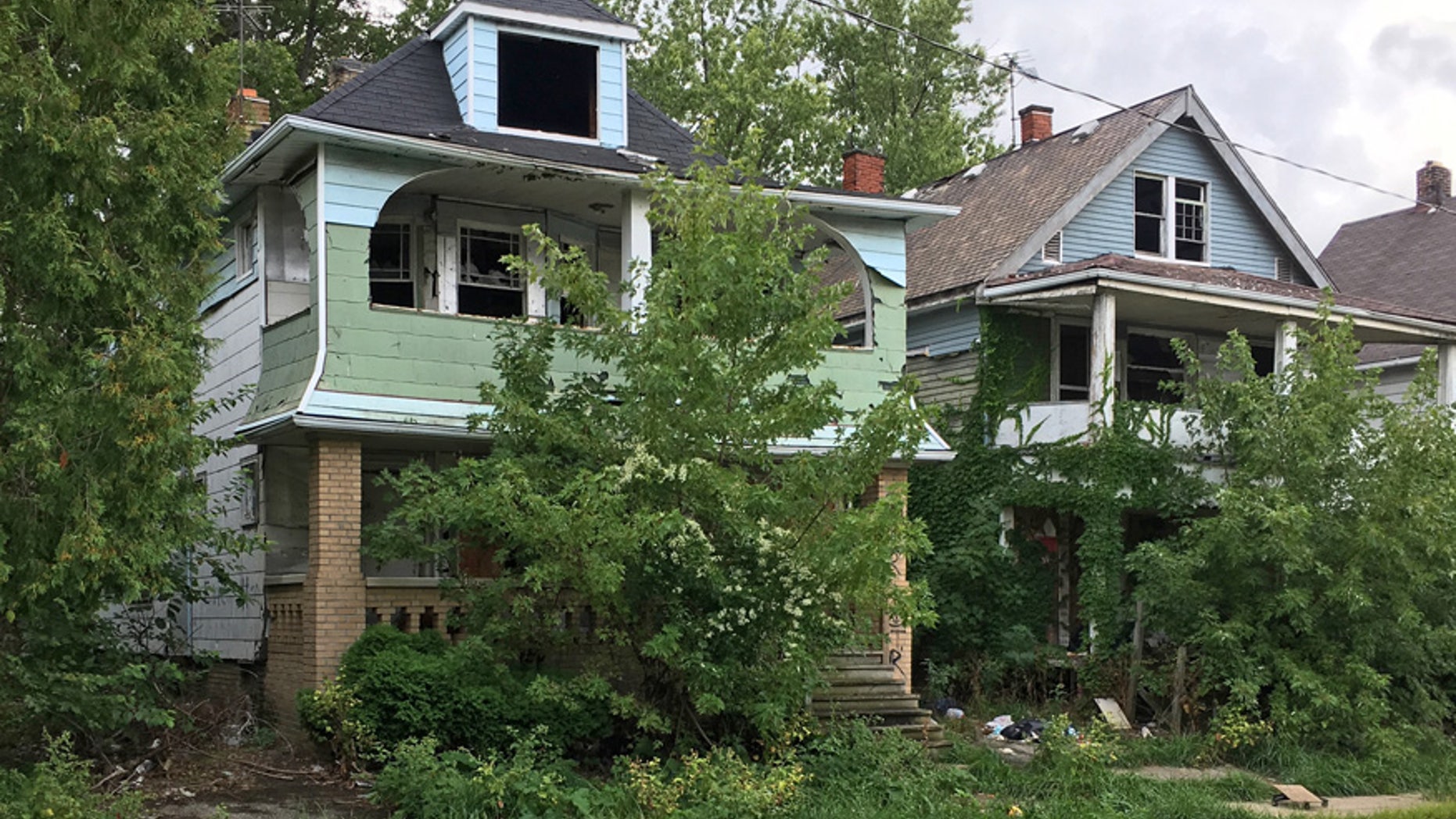 This Aug. 31, 2016, photo shows houses with missing windows and overgrown lawns along a street marred by cracks and potholes in East Cleveland, Ohio. Cleveland and East Cleveland, two of the country's poorest cities, are debating whether to merge, with both cities saying the state of Ohio needs to provide millions to begin fixing East Cleveland's infrastructure and finances.