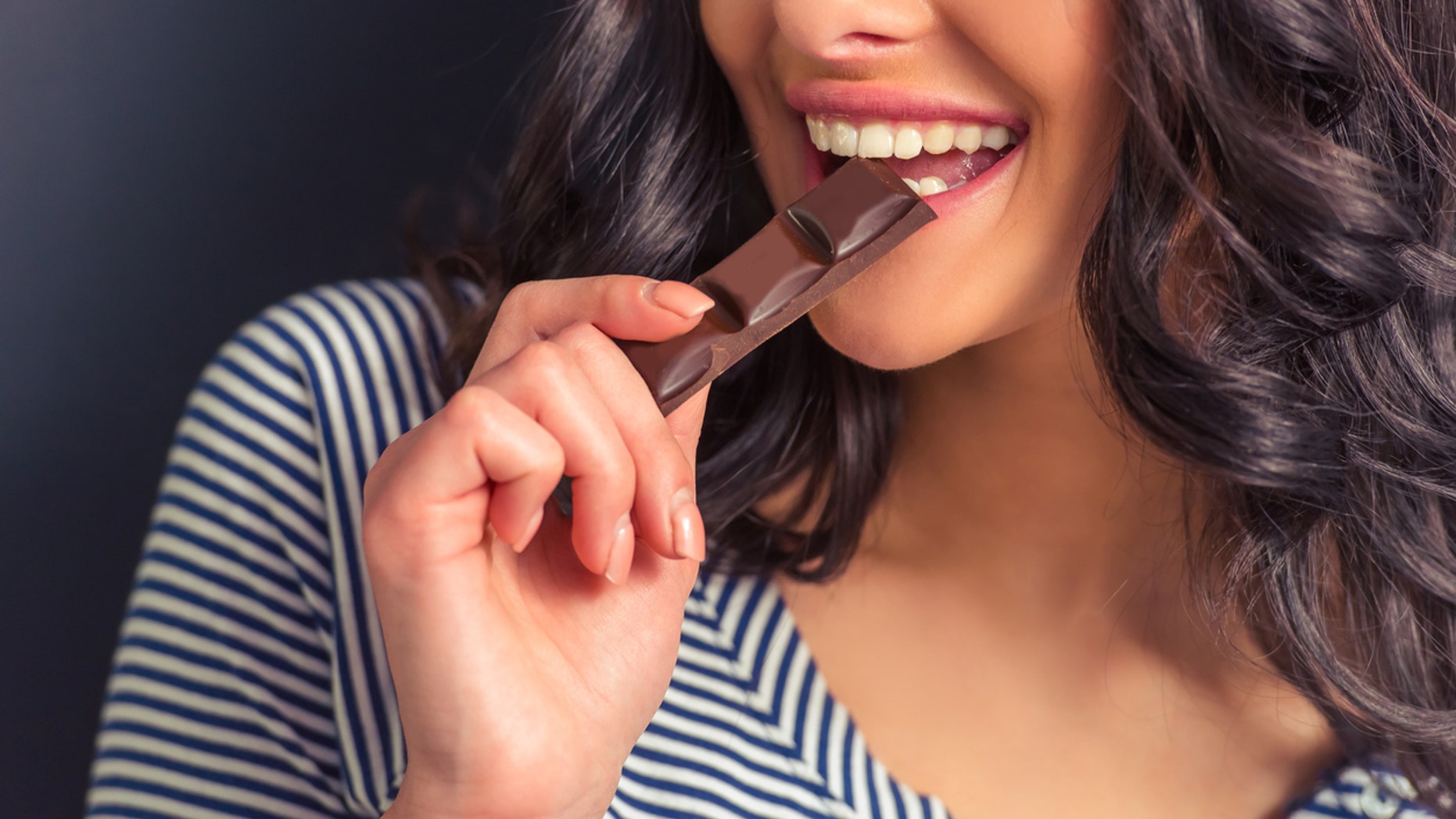 Cropped image of attractive girl eating chocolate and smiling, against dark background