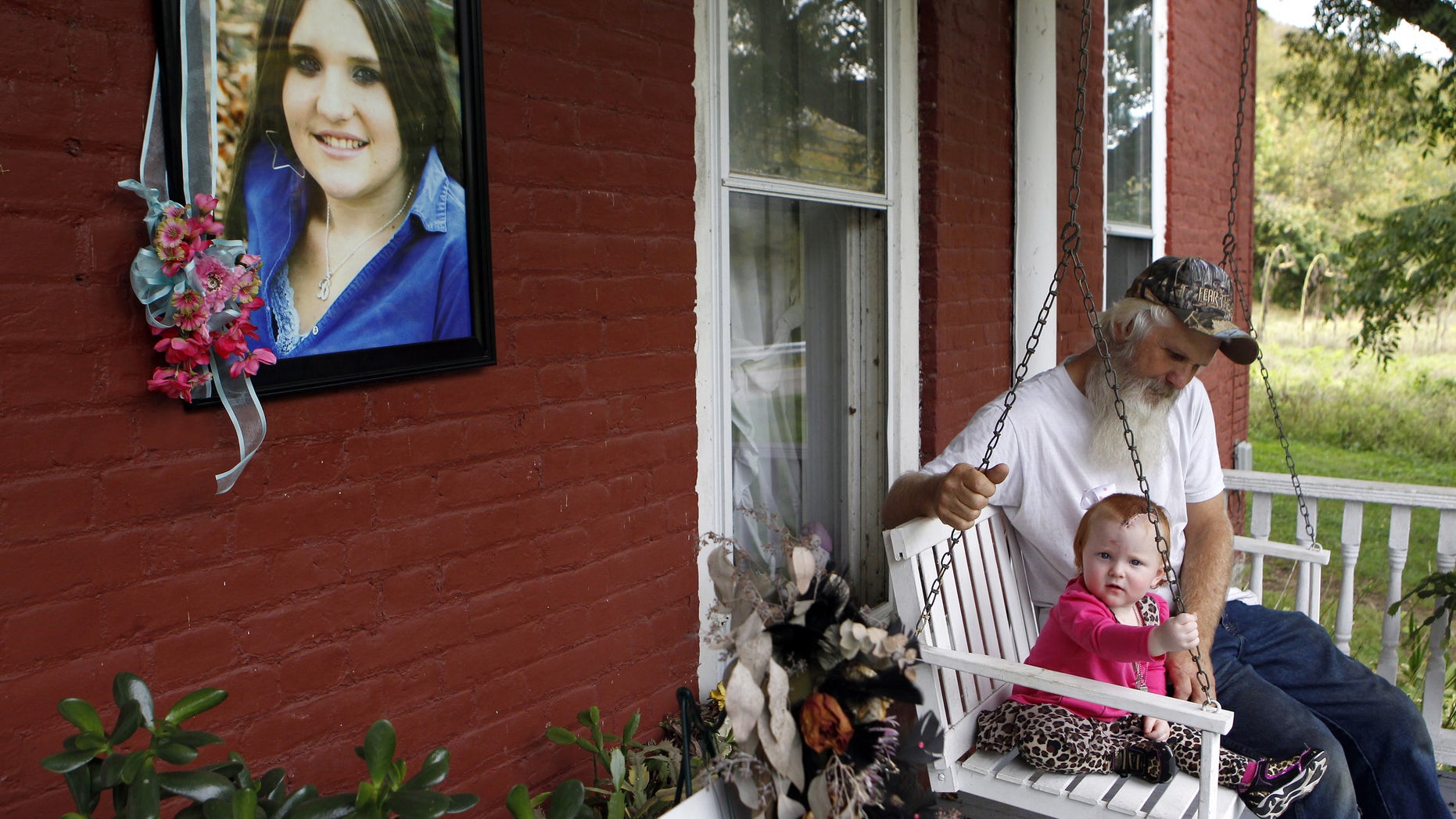 In this October 3, 2013 photo, David Dodson sits with his granddaughter, Aubree Stykes, on the porch of his home in Ripley, Ohio next to a memorial to Dodson's daughter Brittany Stykes, who was killed in an unsolved attack in southern Ohio. Aubree, was shot in the head but has recovered. No arrests have been made, no suspects have been identified and no murder weapon has been found. Mary Dodson says she had hoped her daughter's killing would be solved by the holidays but now she's afraid it never will be. (AP Photo/Cara Owsley, The Enquirer, File)