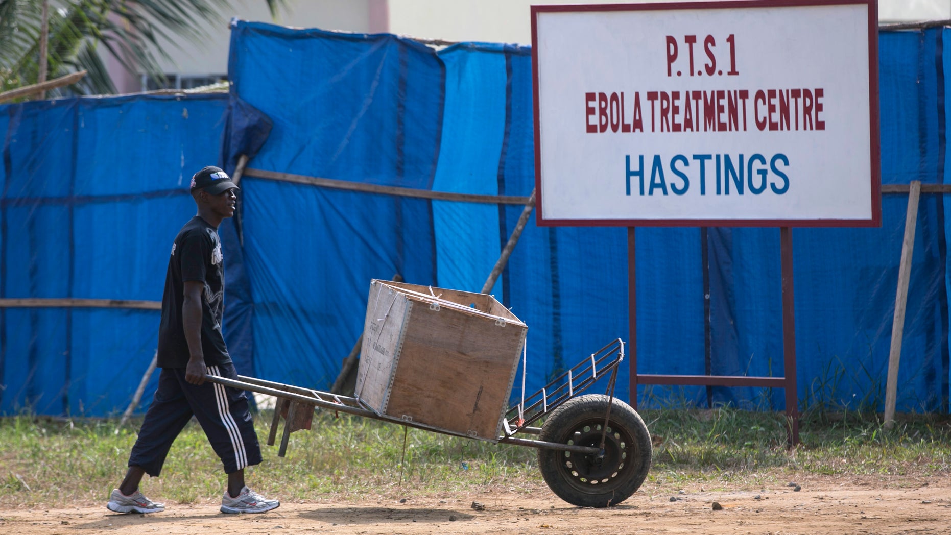 A man pushes a wheelbarrow past the entrance to Hastings Ebola treatment centre in a neighbourhood in Freetown December 21, 2014. REUTERS/Baz Ratner