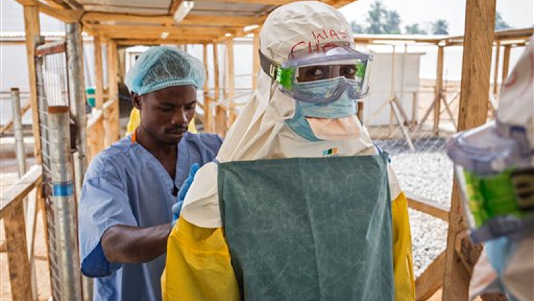 In this photo taken on Monday, March 2, 2015, a health care worker prepares a colleague's virus protective gear before entering a high risk zone at an Ebola virus clinic operated by the International Medical Corps in Makeni, Sierra Leone. (AP Photo/ Michael Duff)