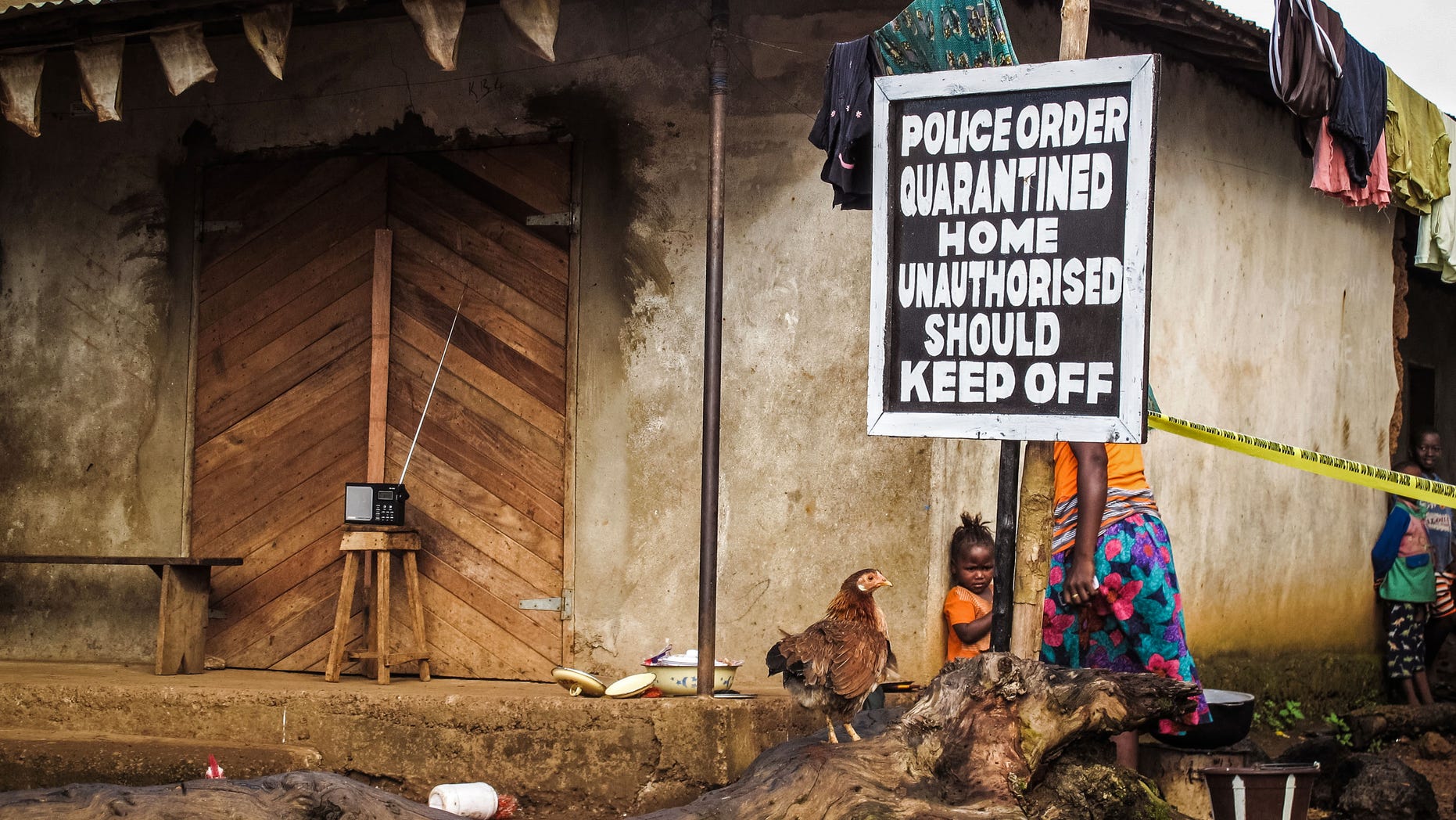 In this file photo taken on Wednesday, Oct. 22, 2014, A child, center, stands underneath a signboard as a family home is placed under quarantine due to the Ebola virus in Port Loko, Sierra Leone. (AP Photo/Michael Duff, File)