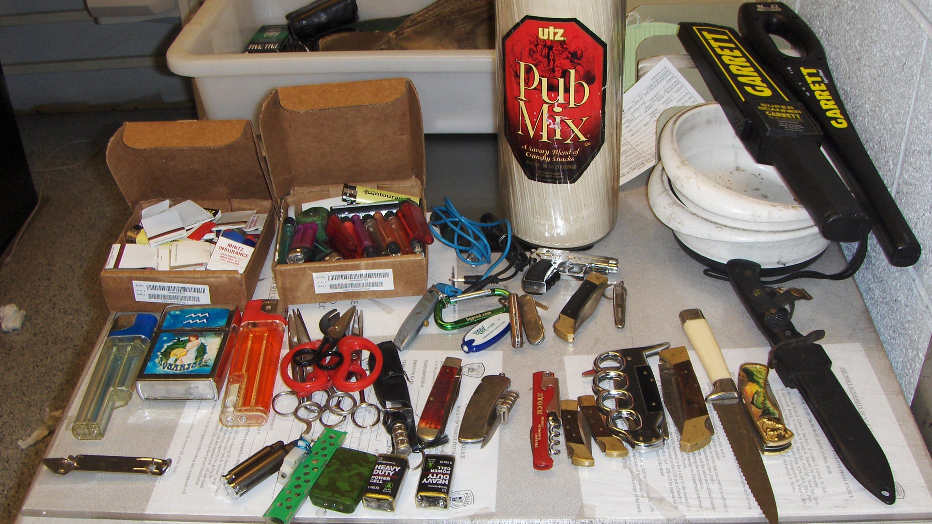 In this photo provided by the Police Department of the Port Authority of New York and New Jersey, a collection of large knives, cigarette lighters, scissors and matches fill a table at the Port Authority Police facility located in the John F. Kennedy International Airport in the Brooklyn Borough of New York, Saturday, Oct. 19, 2013. The items were sized after an airport baggage screener noticed the items in a person’s carry-on bag. The Port Authority Police arrested Timothy Schiavo, Jr., 29, Patchogue NY and charged him with criminal possession of a weapon. (AP Photo/Port Authority Police Department of New York and New Jersey)