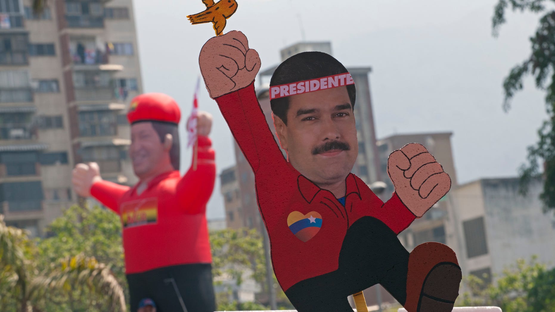 A drawing of ruling party candidate Nicolas Maduro with a bird on his fist with an inflatable doll of the late Hugo Chavez in the background is held up as supporters move to the site of Maduro's closing campaign rally in Caracas, Venezuela, Thursday, April 11, 2013. Maduro, Chavez's hand-picked successor, assured last week during a campaign rally that Venezuela's late President Hugo Chavez's spirit appeared to him in the form of a little bird that flew around his head inside a wooden chapel to give him his blessing. He is running for president against opposition candidate Henrique Capriles in the presidential election set for Sunday, April 14. (AP Photo/Ramon Espinosa)