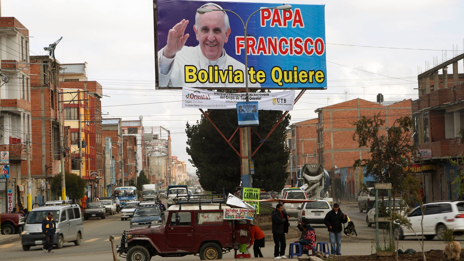 FILE - In this April 16, 2015, file photo, street food vendors set up their stand under a billboard featuring Pope Francis with a message that reads in Spanish; "Pope Francis, Bolivia loves you," in El Alto, Bolvia. Pope Francis' three-nation trip to South America that includes Ecuador, Bolivia and Paraguay, is set for July 6-12, though he will only spend six hours in Bolivia's capital due to the altitude, church officials say. (AP Photo/Juan Karita, File)