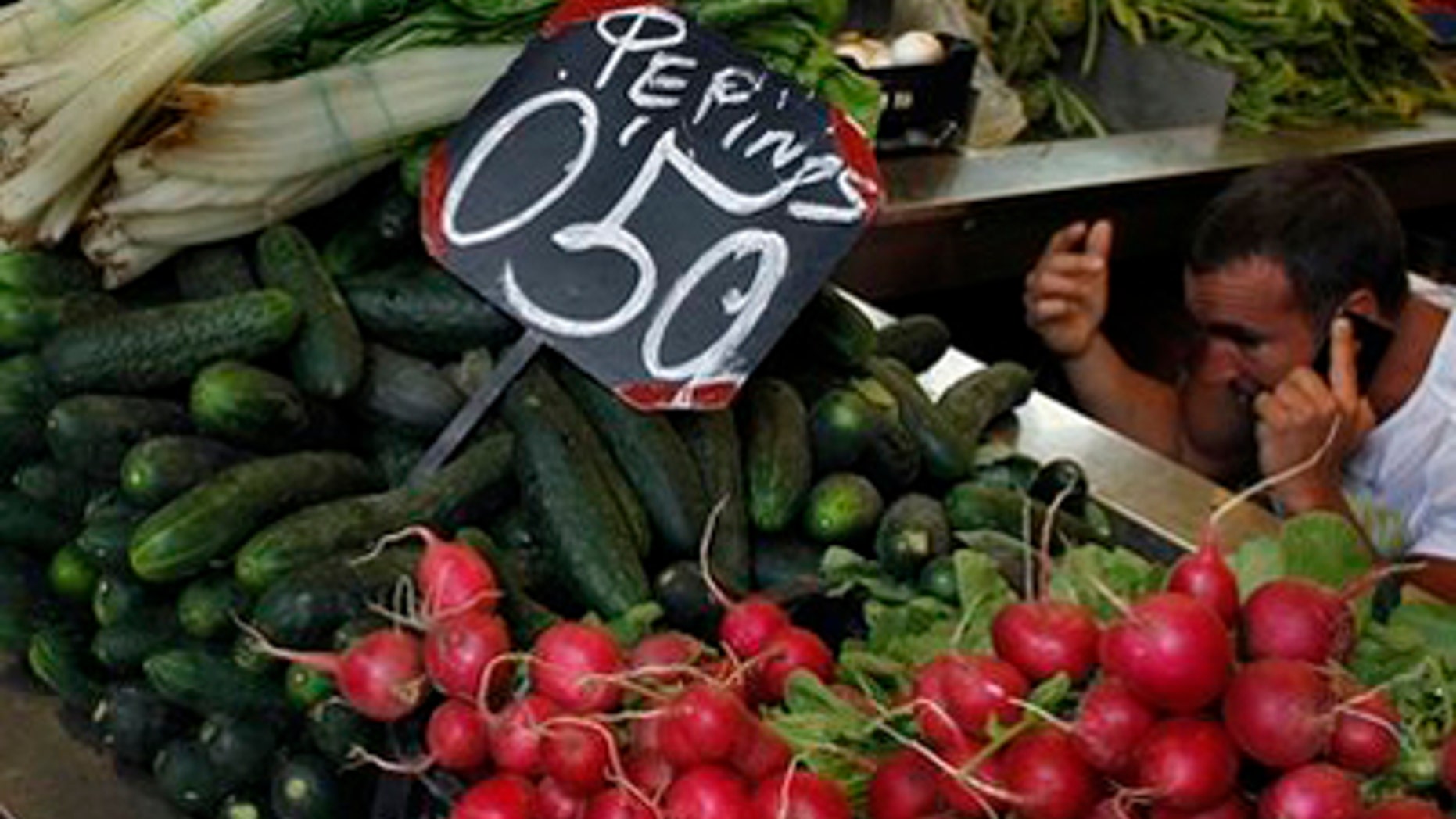A market seller speaks on his cell phone behind a display of cucumbers and other vegetables in Malaga, southern Spain, Monday May 30, 2011. Vegetables from Spain are suspected of carrying the dangerous E.coli bacteria, which is suspected of killing some people in Germany and has caused many hundreds of people to become ill across Europe. Austria has moved to ban the sale of cucumbers, tomatoes and eggplants that originated from Spain, although Spanish authorities said there is no proof that they are the source of the outbreak.