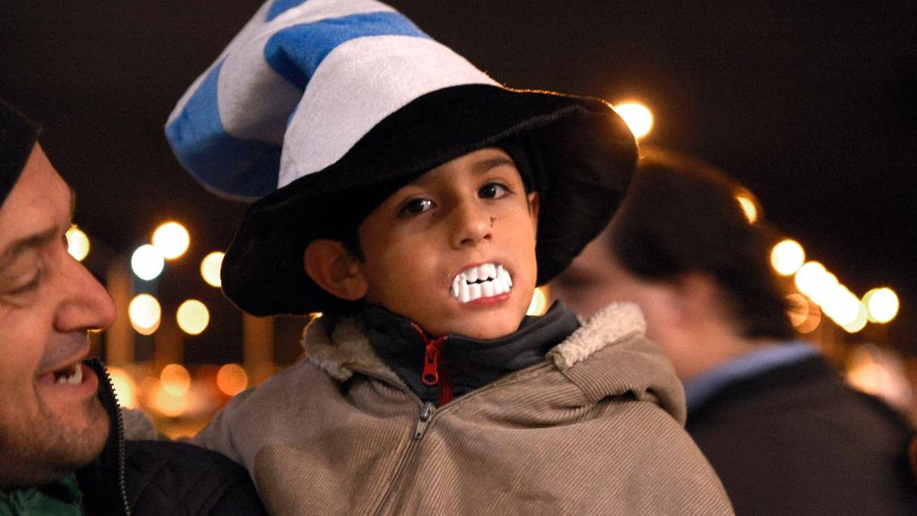 A child shows his support for Uruguay player Luis Suarez, by wearing toy plastic vampire's teeth, as he awaits the arrival of Suarez at Carrasco International Airport in the outskirts of Montevideo, Uruguay, Thursday, June 26, 2014. The Uruguay forward, widely regarded as one of the best players in the world, was banned by FIFA from all football for four months on Thursday for biting an Italian opponent in an incident that marred the team's victory and progression to the second round. (AP Photo/Matilde Campodonico)