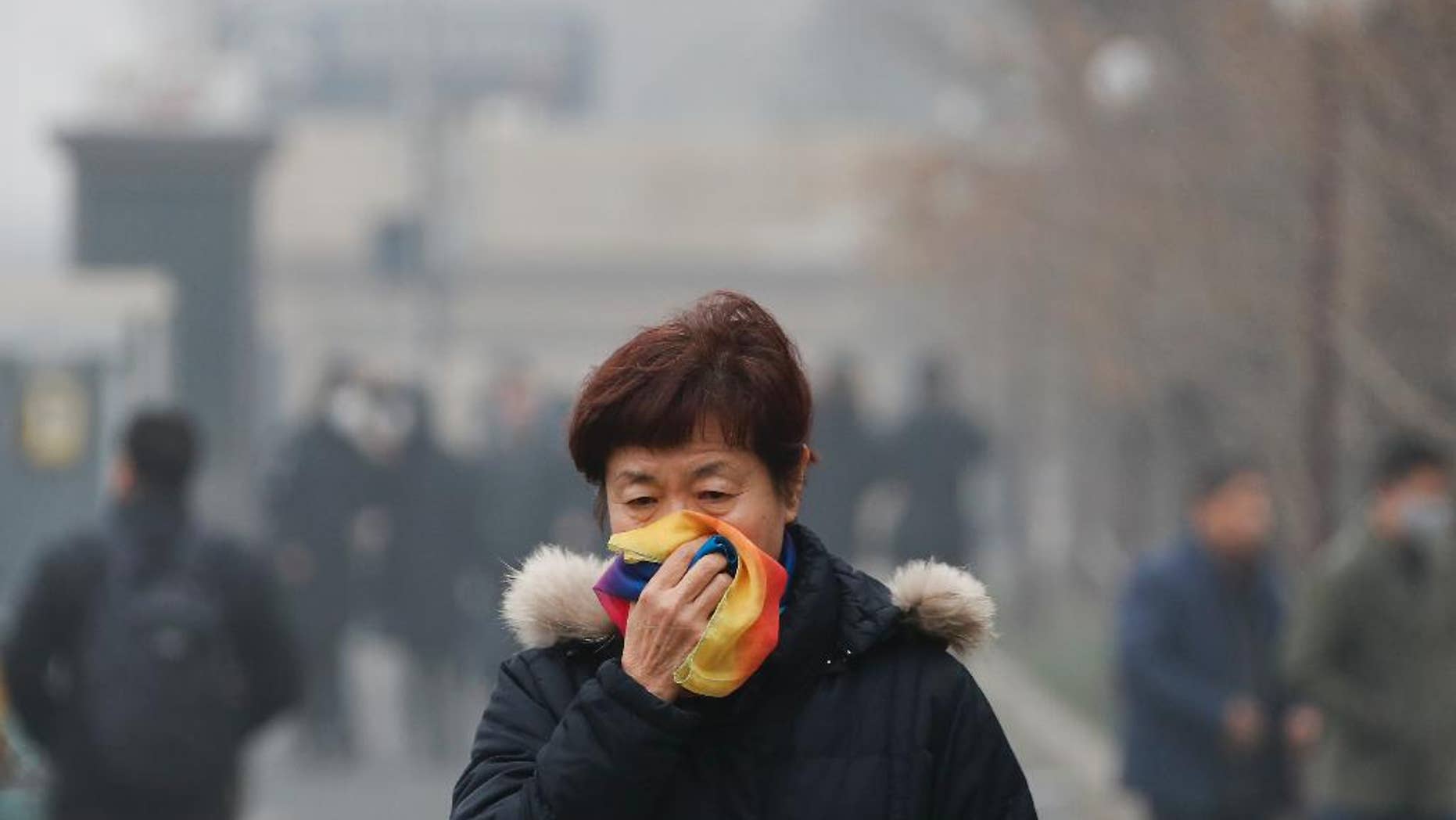 FILE - In this Tuesday, Dec. 20, 2016, file photo, a woman uses a scarf to cover her mouth for protection against the air pollution as she walks on a street in Beijing, China. Beijing will spend $2.7 billion to fight air pollution in the capital this year, state media reported Thursday. (AP Photo/Andy Wong, File)