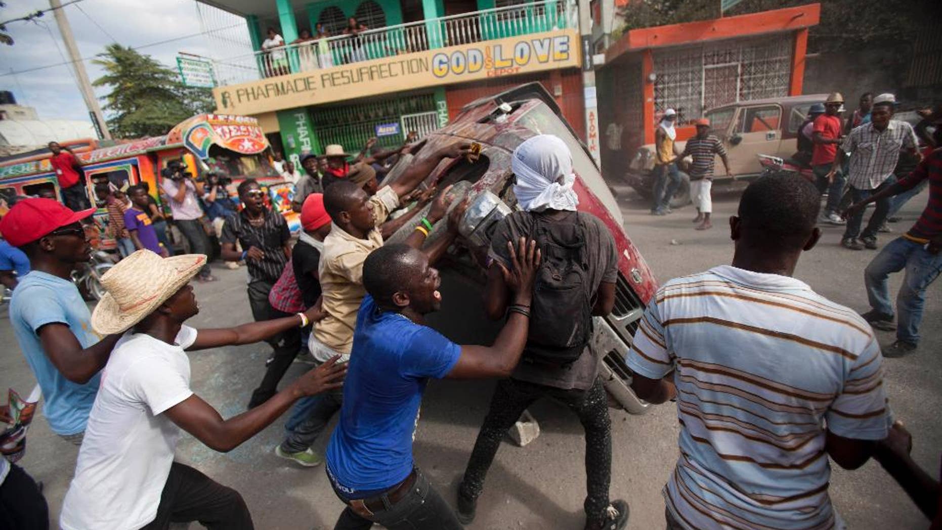 FILE - This Jan. 11, 2015 file photo shows demonstrators flipping a car to block off a street during a protest demanding the resignation of President Michel Martelly in Port-au-Prince, Haiti, while the president and opposition officials were locked again in negotiations trying to forge a last-minute deal to resolve a standoff that's stalling elections. The political turmoil has been brewing since shortly after Martelly took office in 2011 as a newcomer to politics with little support in parliament, which is critical in a country where the constitution deliberately curbs executive power. (AP Photo/Dieu Nalio Chery, File)