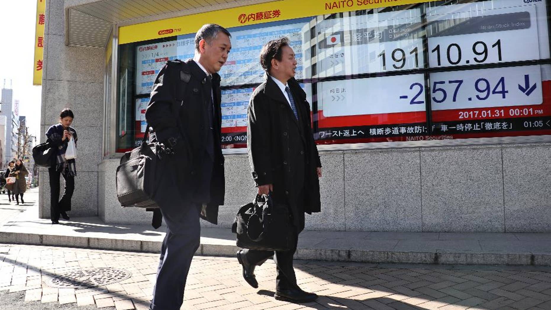 Men walk past an electronic stock indicator of a securities firm in Tokyo, Tuesday, Jan. 31, 2017. Asian shares slipped Tuesday, tracking a decline on Wall Street set off by jitters over President Donald Trump's travel ban. (AP Photo/Shizuo Kambayashi)