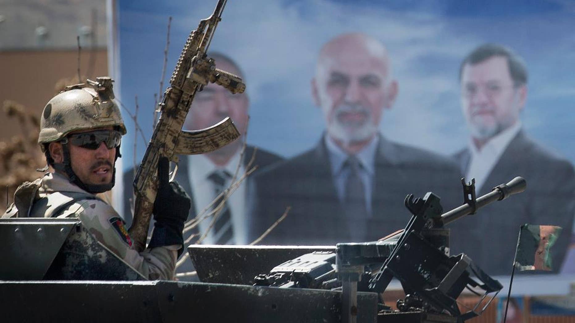 An Afghan special forces soldier takes up position next to an election campaign poster of presidential candidate Ashraf Ghani Ahmadzai, center on the poster, after the Taliban launched an assault with a suicide bomber detonating his vehicle outside an election office in Kabul, Afghanistan, Tuesday, March 25, 2014. Gunmen stormed into the building, trapping dozens of employees inside and killing many people. A candidate for a seat on a provincial council was among those killed, along with an election worker, a civilian and a policeman. (AP Photo/Anja Niedringhaus)