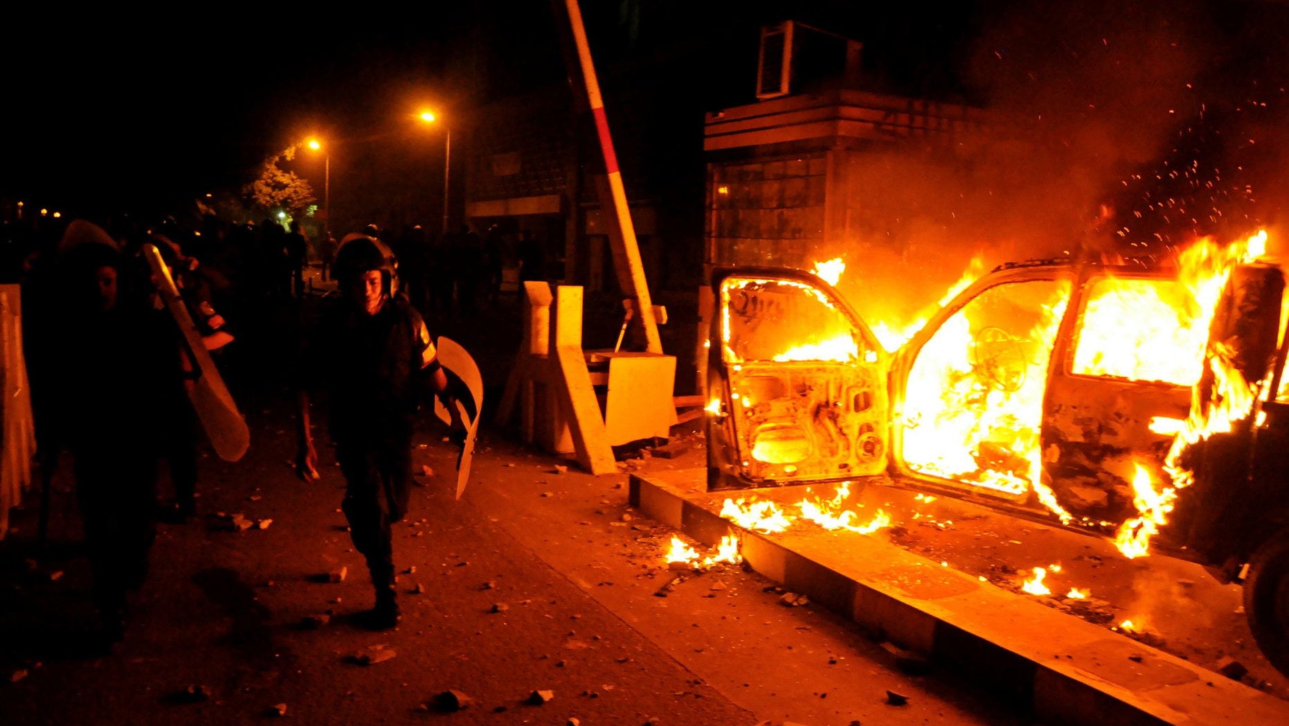 A riot policeman passes burning vehicles during clashes outside the U.S. embassy in Cairo, Egypt, early Thursday, Sept. 13, 2012, as part of widespread anger across the Muslim world about a film ridiculing Islam's Prophet Muhammad. (AP Photo/Hussein Tallal)