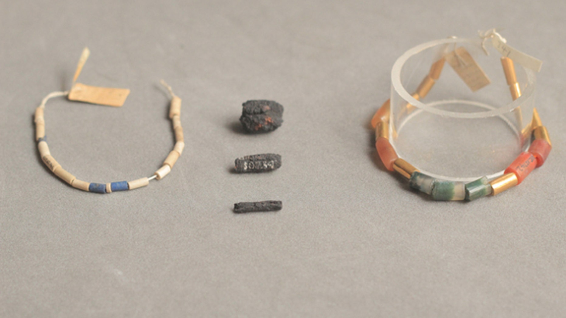 Meteoric iron beads (center) are pictured between ancient Egyptian necklaces that are strung with tube-shaped lapis lazuli (blue), carnelian (brownish/red), agate, and gold beads.