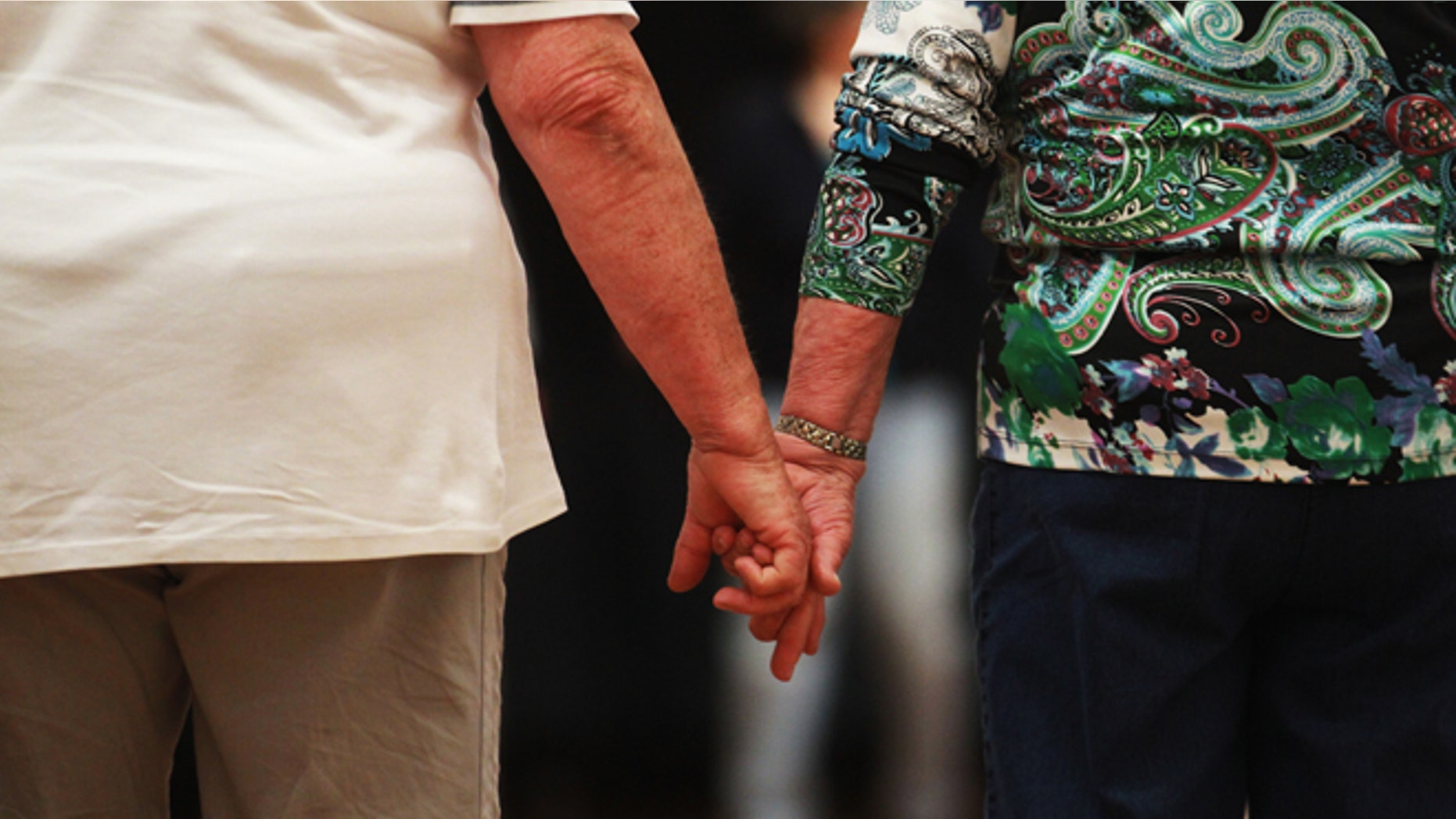 HAMBURG, GERMANY - MAY 03: An elderly couple hold hands at a trade fair at the âSeniorentag 2012â senior citizens convention on May 3, 2012 in Hamburg, Germany. The three-day long convention caters specifically to the needs of elderly people, who in Germany, as in the rest of Europe, are becoming an increasingly higher portion of the overall population. Europe as a whole, through its low birth rates and improving health care, is undergoing a demographic shift that has far-reaching consequences for labor markets, public policy planning and government budgets. (Photo by Joern Pollex/Getty Images)