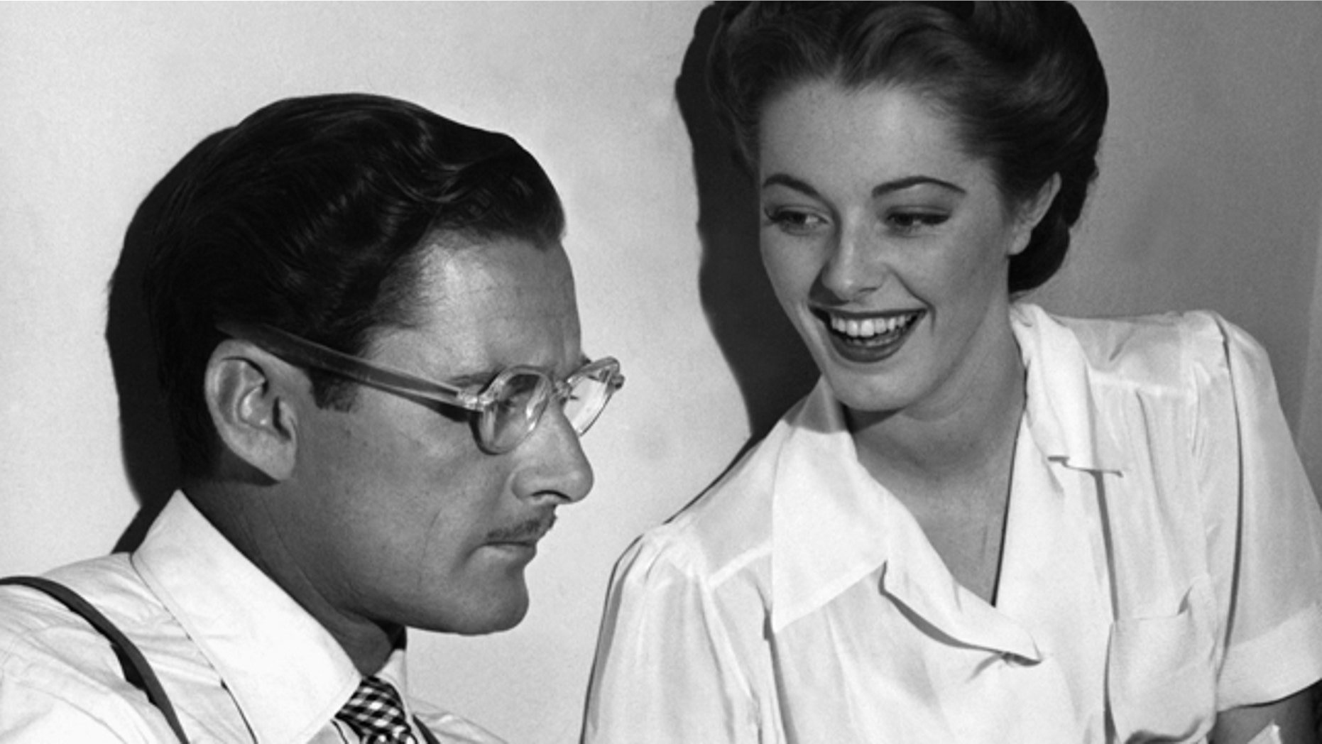 Errol Flynn seems to be in a literary mood as, between takes on the set of "Never Say Goodbye," he reads an amusing passage from a new novel to his leading lady, Eleanor Parker, who appears to enjoy the presentation in Los Angeles.