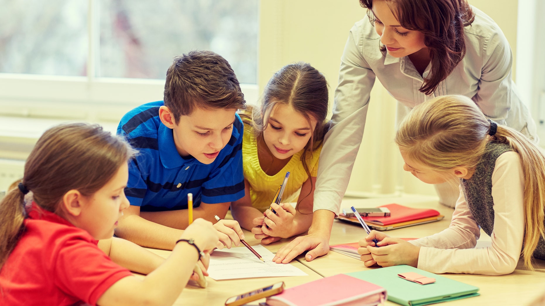 education, elementary school, learning and people concept - teacher helping school kids writing test in classroom
