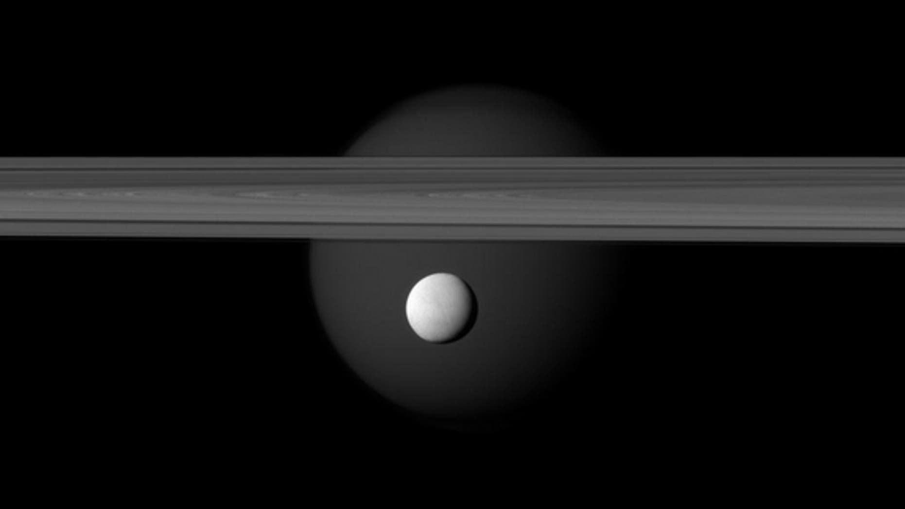 Saturn’s icy moon Enceladus hangs below the gas giant’s rings while Titan lurks in the background, in this new image taken by the Cassini spacecraft on March 12, 2012.