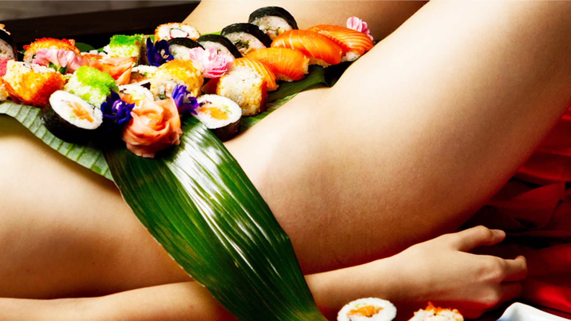 Sushi on a woman's nude stomach with banana leafs on young woman