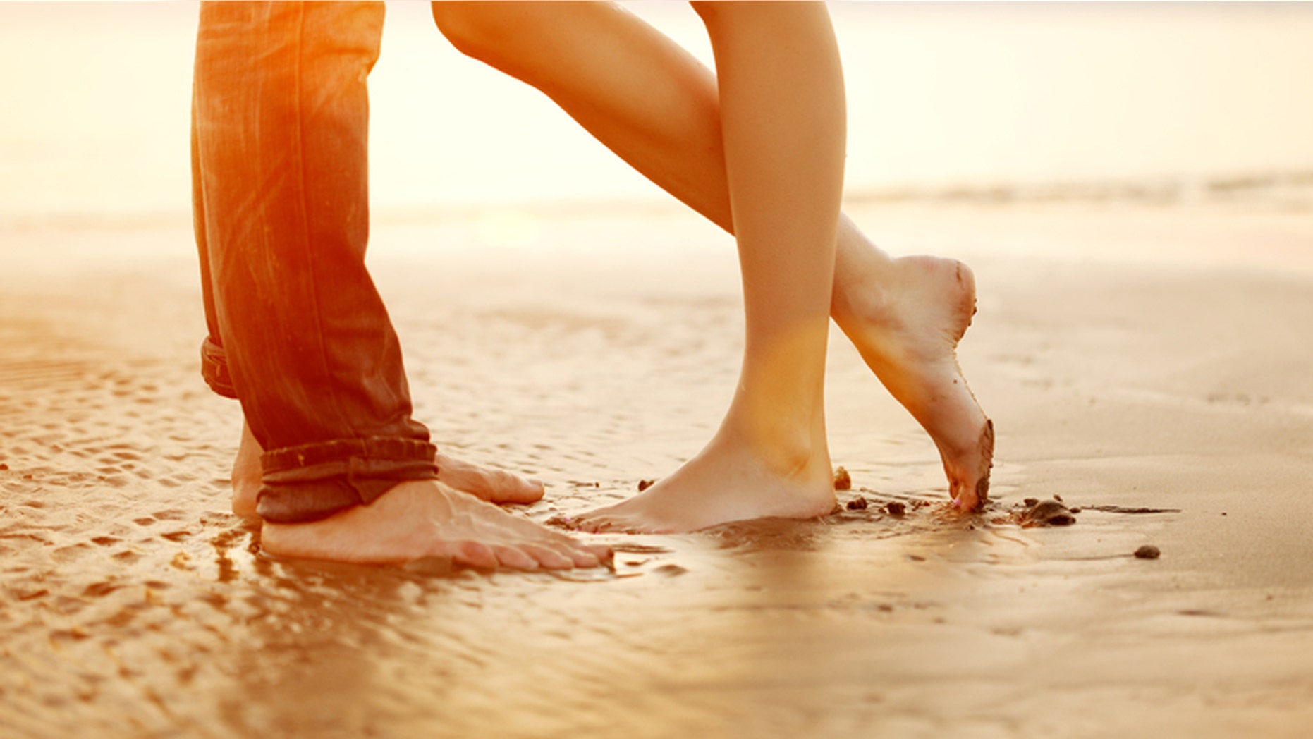 A young loving couple hugging and kissing on the beach at sunset. Two lovers, man and woman barefoot near the water. Summer in love