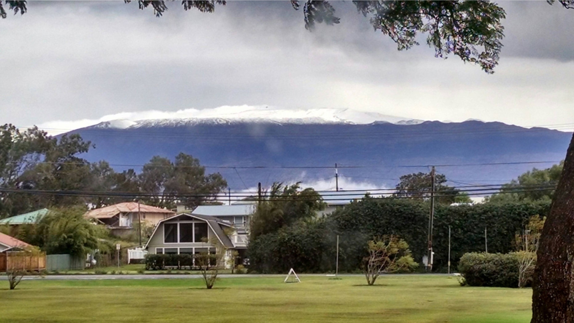 This photo provided by Grant Matsushige, an Instrumentation Specialist at the Canada-France-Hawaii Telescope, shows the summit of Mauna Kea on Hawaii's Big Island covered in snow as seen from Waimea, Hawaii on Thursday, Dec. 1, 2016. The National Weather Service in Honolulu has issued a winter storm warning for the summits of Hawaii's Big Island as wind and snow engulf the high peaks. (Grant Matsushige/Canada-France-Hawaii Telescope via AP)