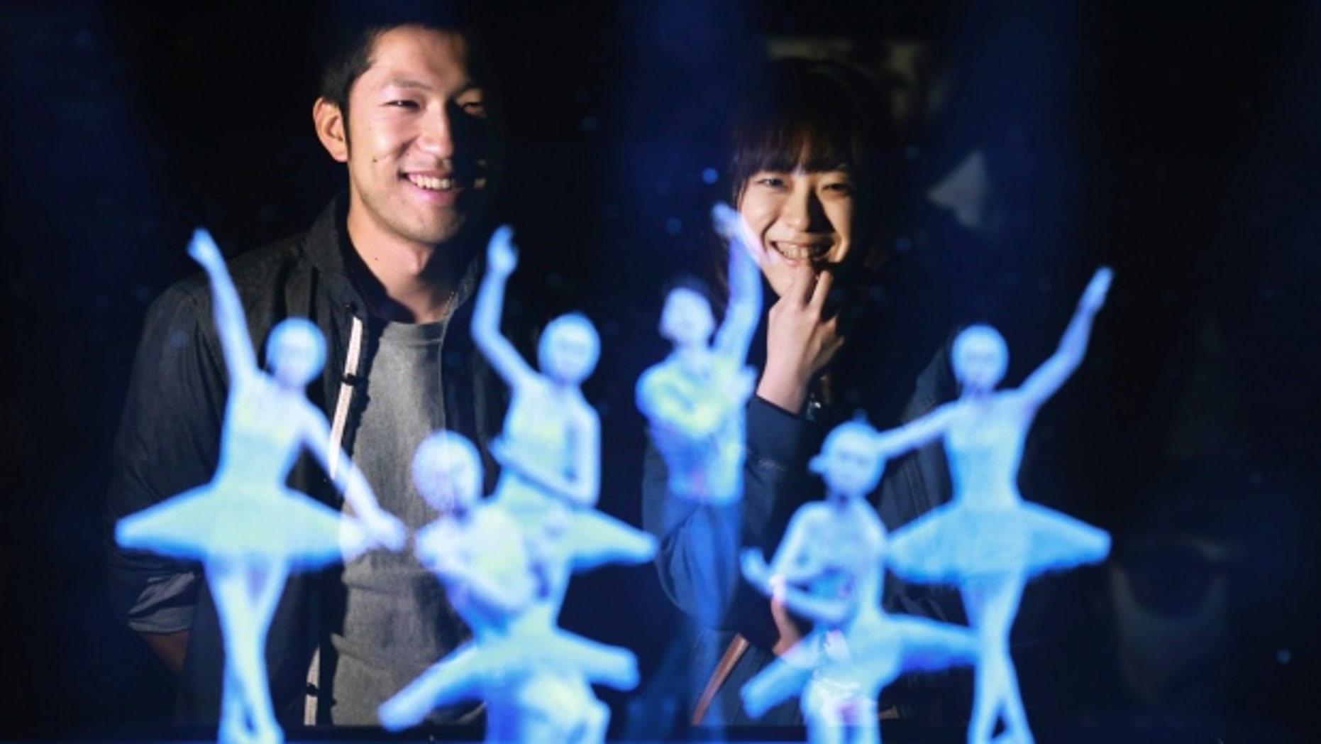 Tomoaki Ishizuka, left, and Yurika Yonekura, right, watch the hologram of Japanese skater Yuzuru Hanyu, center, with ballet dancers with their scanned faces attached at newly opened Hologram Dance Theater at Madame Tussauds in Tokyo, Japan.