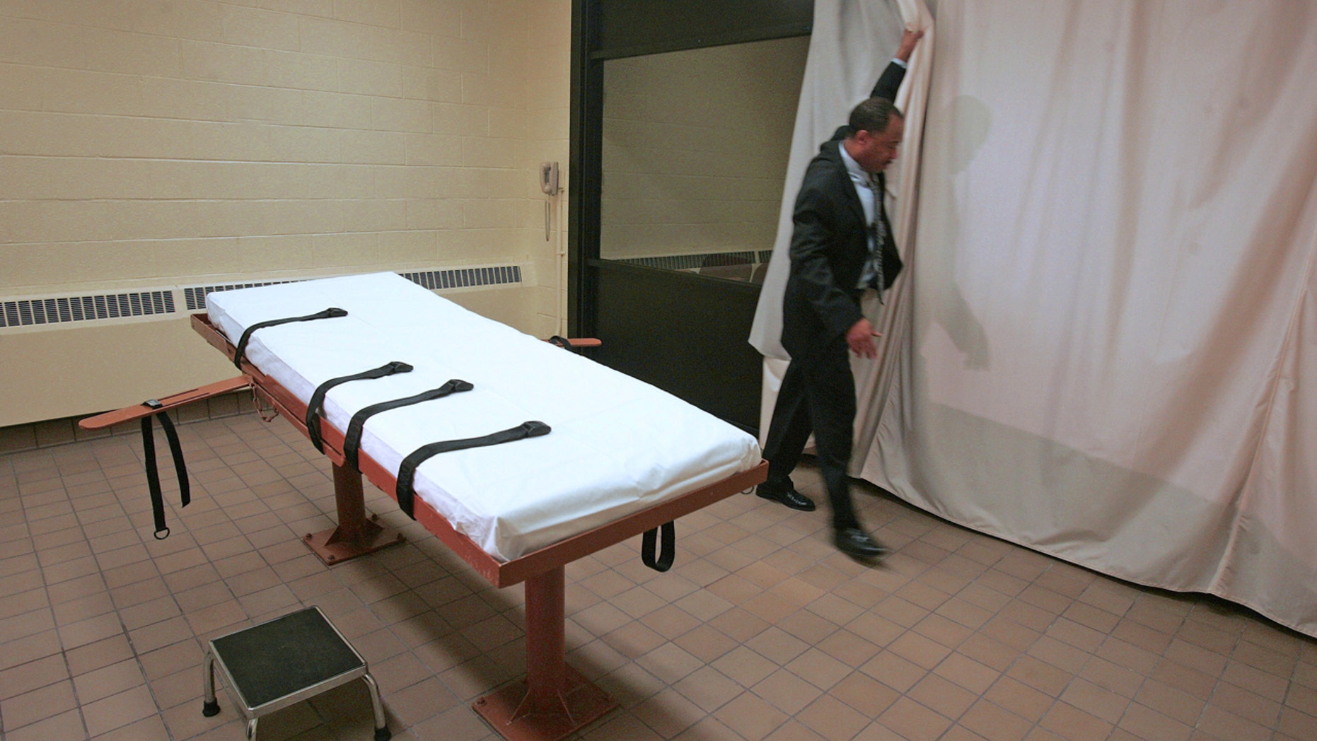 FILE – In this November 2005 file photo, Larry Greene, public information director of the Southern Ohio Correctional Facility, demonstrates how a curtain is pulled between the death chamber and witness room at the prison in Lucasville, Ohio.