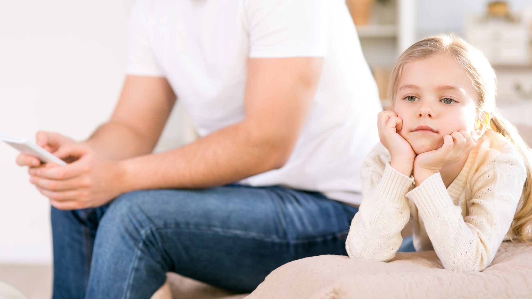 Play with me. Close up of moody little girl sitting on the sofa with her father holding mobile phone while going to make a call