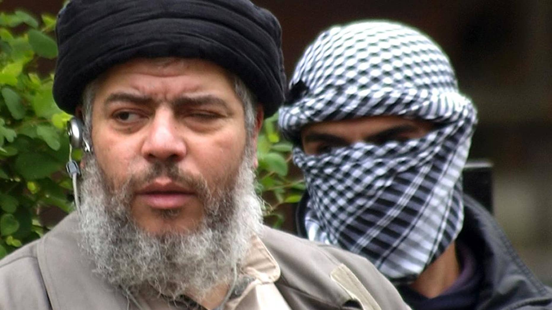 FILE - In this April 30, 2004 file photo, Muslim cleric Mustafa Kamel Mustafa arrives with a masked bodyguard to conduct Friday prayers in the street outside the closed Finsbury Park Mosque in London. The 55-year-old Egyptian cleric, who also goes by the alias Abu Hamza al-Masri, was found guilty on Monday, May 19, 2014 in federal court in New York of providing material support to terrorist organizations. (AP Photo/Max Nash, File)