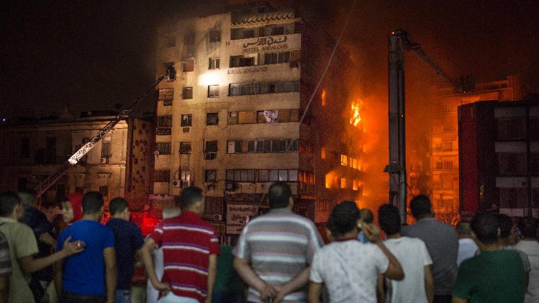 People look at a fire that erupted inside a six-story hotel called Andalusia in the populous Ataba neighborhood in Cairo, Egypt, Monday, May 9, 2016. A massive fire erupted early hours Monday morning in a busy low-price commercial area in downtown Cairo, injuring at least 60 mostly from suffocation. There were no reports of deaths. (AP Photo/Sabry Khaled)