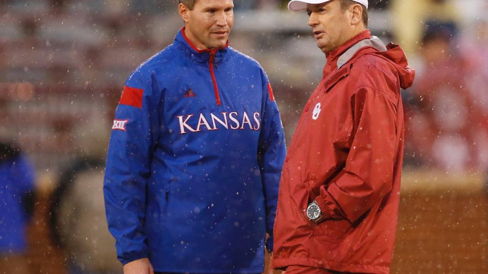 Kansas head coach Clint Bowen, left, and Oklahoma head coach Bob Stoops, right, talk before the start of their weather delayed NCAA college football game in Norman, Okla., Saturday, Nov. 22, 2014. The start time was pushed back at least 90 minutes due to lightning. (AP Photo/Sue Ogrocki)
