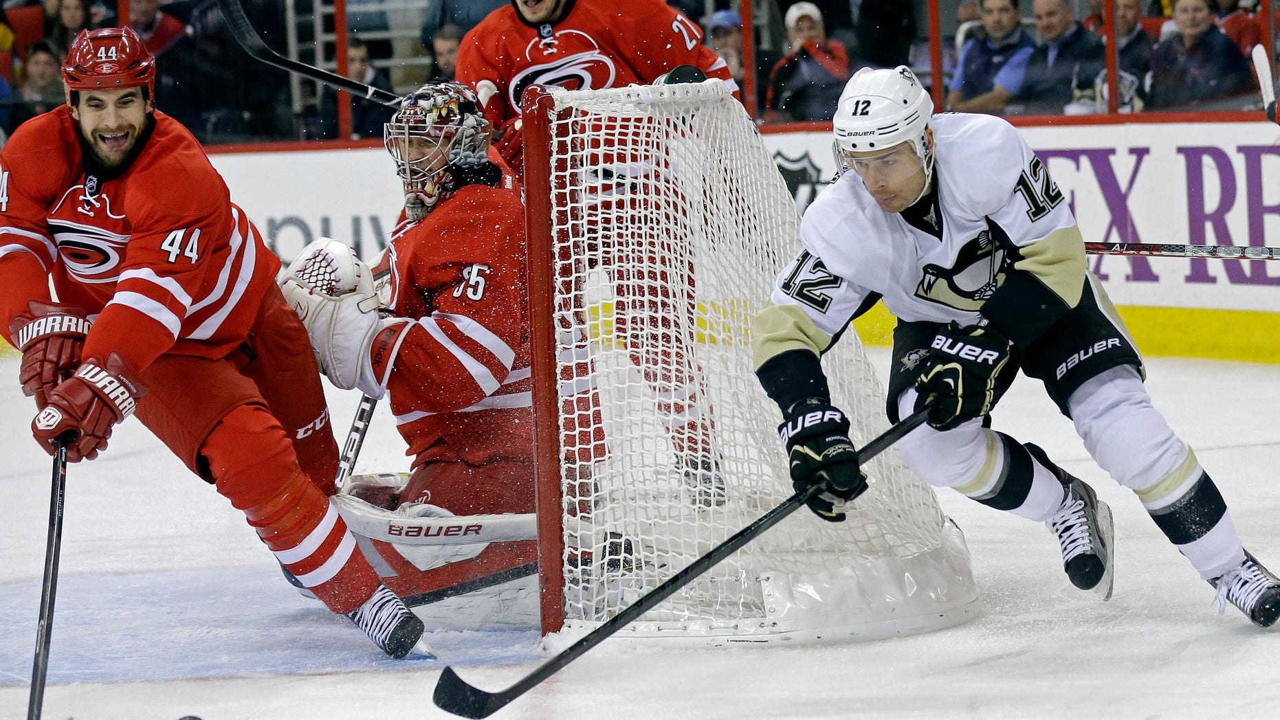 Pittsburgh Penguins' Chuck Kobasew (12) and Carolina Hurricanes' Jay Harrison (44) reach for the puck as Hurricanes goalie Justin Peters (35) defends the goal during the first period of an NHL hockey game in Raleigh, N.C., Monday, Oct. 28, 2013. (AP Photo/Gerry Broome)