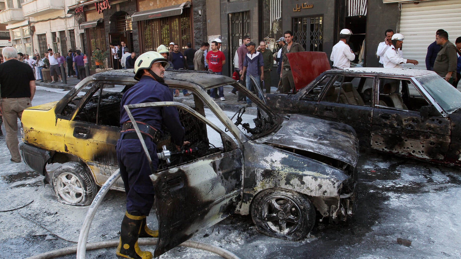 Firefighters extinguish a burning vehicle after two mortar rounds struck the Abu Roumaneh area in Damascus, Syria, Saturday, Oct. 12, 2013. Syria’s state news agency said two mortar rounds struck an upscale neighborhood in the Syrian capital of Damascus, killing at least one child and injuring a dozen people. (AP Photo)