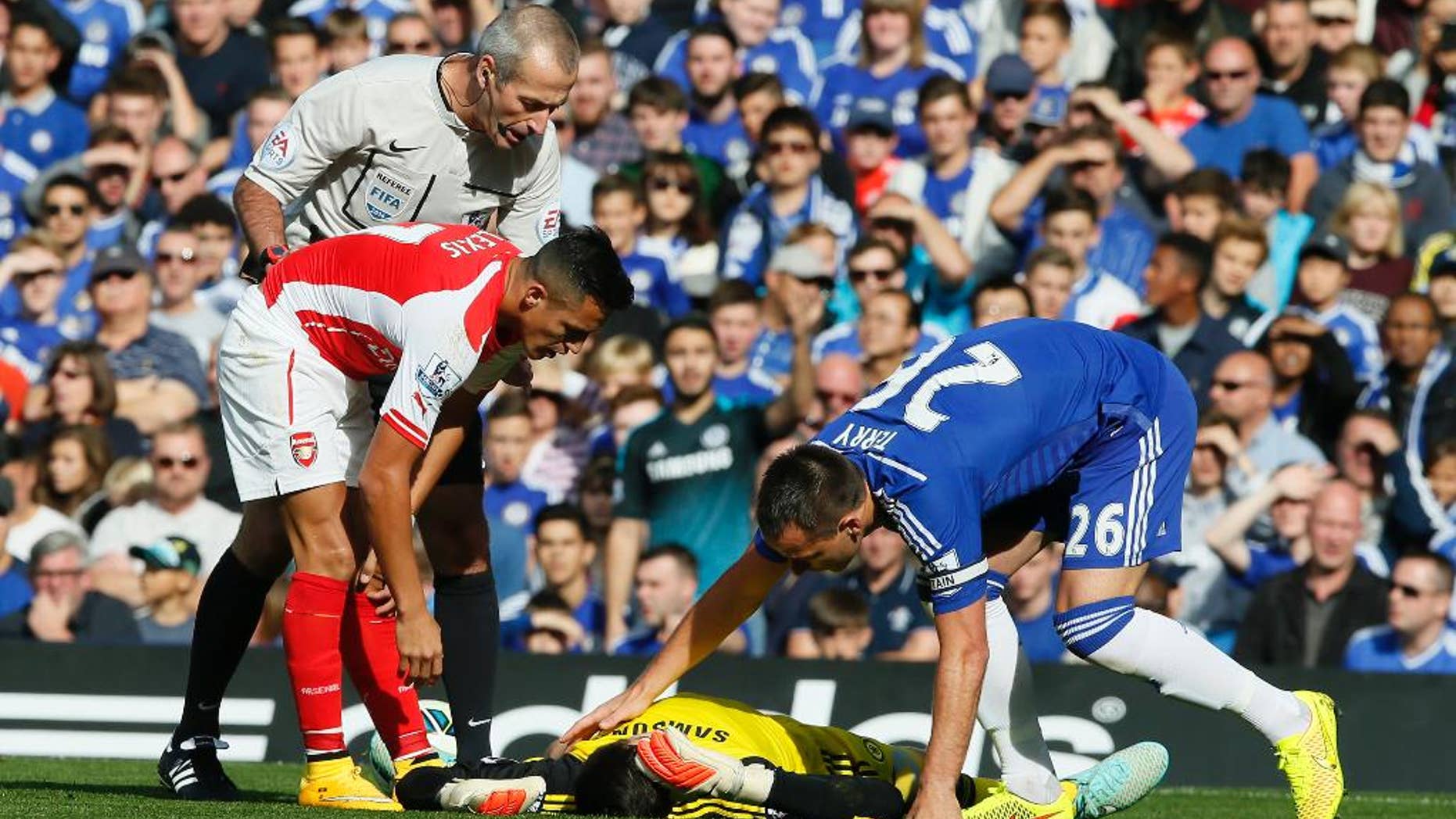 Arsenal's Alexis Sanchez, left, gets up after colliding with Chelsea's goalkeeper Thibaut Courtois, who lies on the ground attended to by teammate Chelsea's John Terry, right, during their English Premier League soccer match between Chelsea and Arsenal at Stamford Bridge stadium in London Sunday, Oct. 5, 2014. (AP Photo/Alastair Grant)