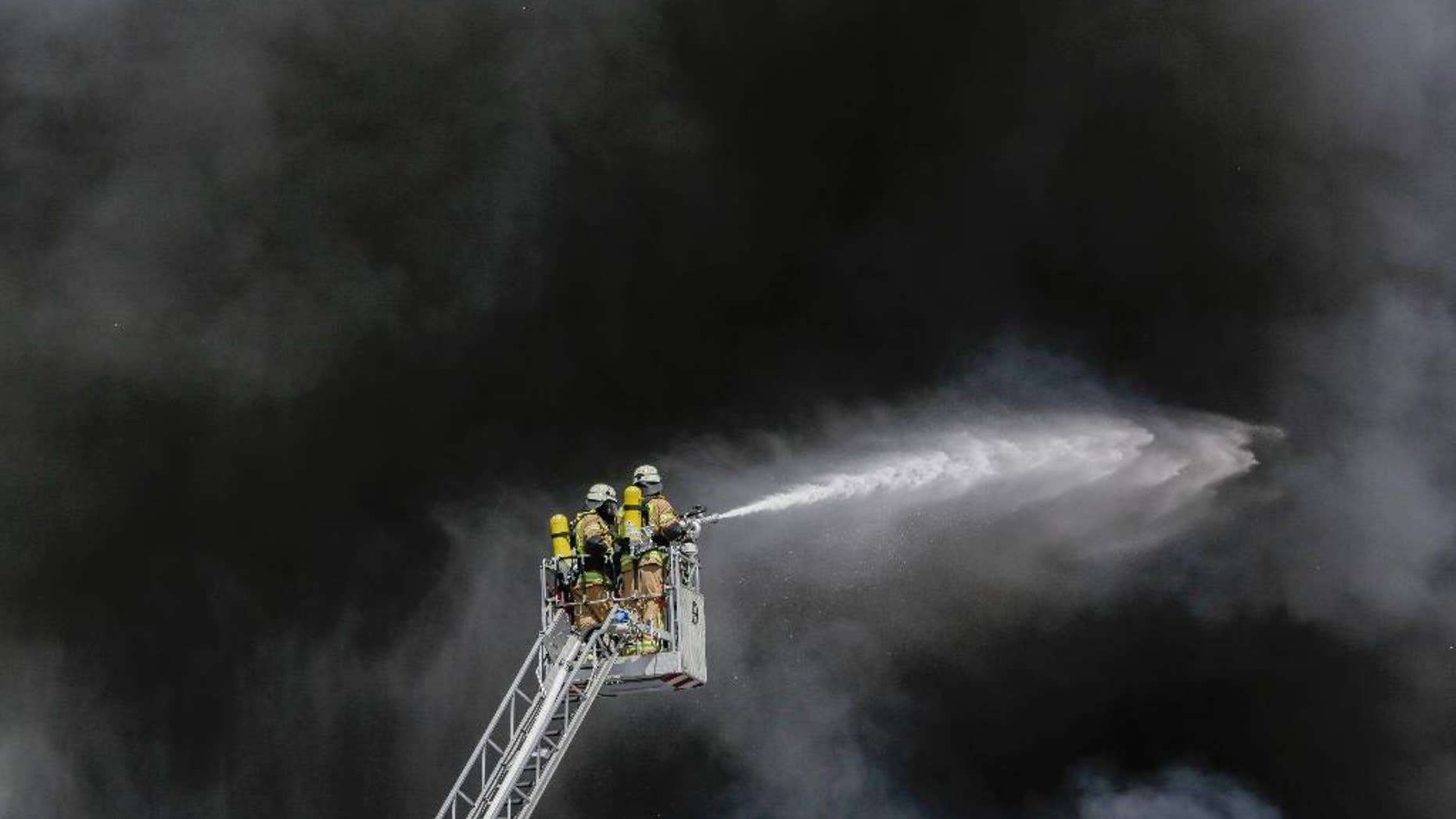 Fire fighters spray water in front of smoke at a burning storage hall of the Dong Xuan Center, an Asia market specialized in Vietnamese goods, in Berlin, Germany, Wednesday, May 11, 2016. The fire department sent some 150 trucks and other vehicles to the fire which broke out Wednesday morning . (AP Photo/Markus Schreiber)