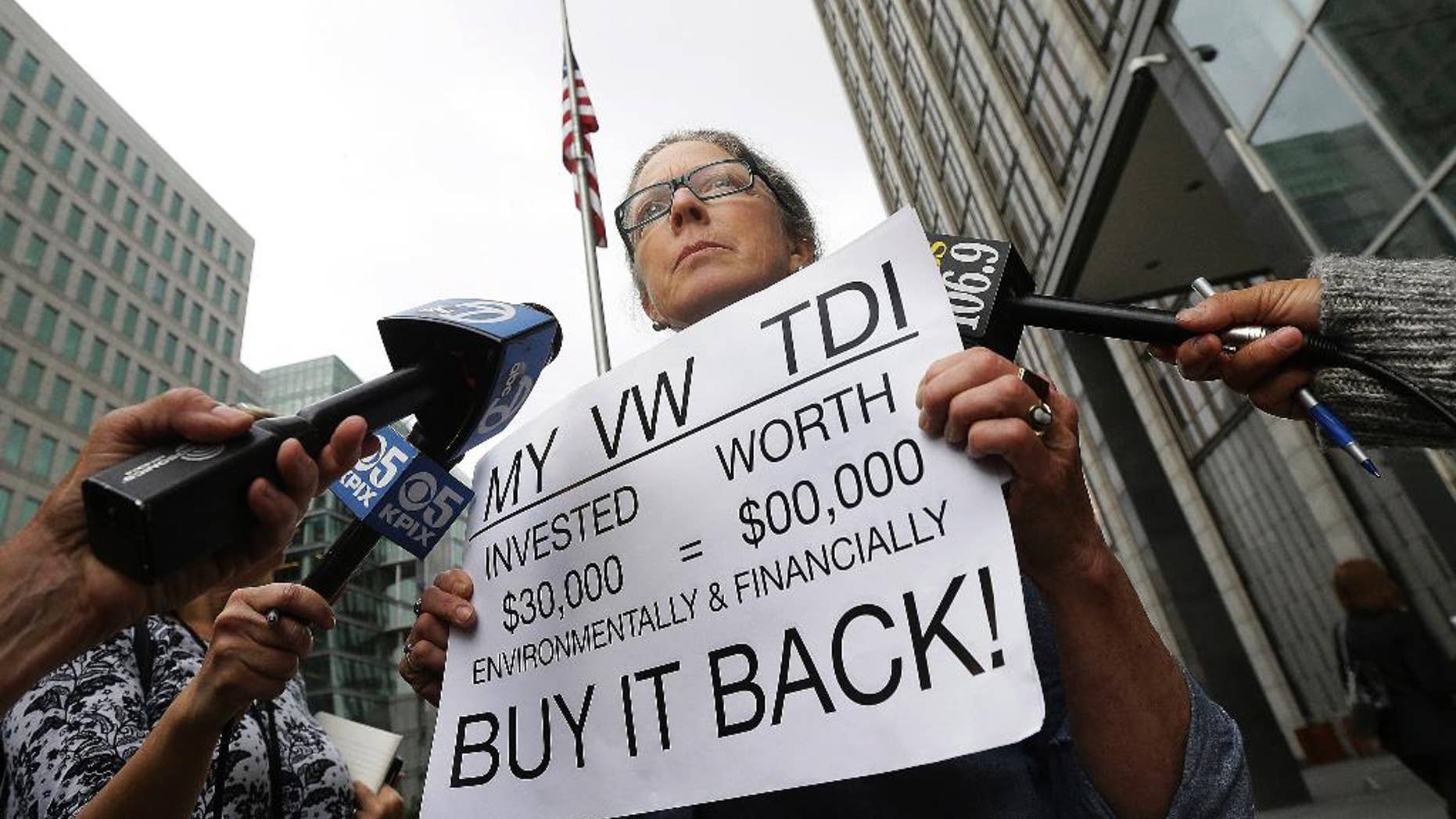 Joyce Ertel Hulbert, owner of a 2015 Volkswagen Golf TDI, holds a sign while interviewed outside of the Phillip Burton Federal Building in San Francisco, Thursday, April 21, 2016. An agreement will give consumers who bought nearly 600,000 Volkswagen vehicles rigged to cheat on emissions tests the option of having the automaker buy back the cars or fix them, a judge said Thursday. (AP Photo/Jeff Chiu)