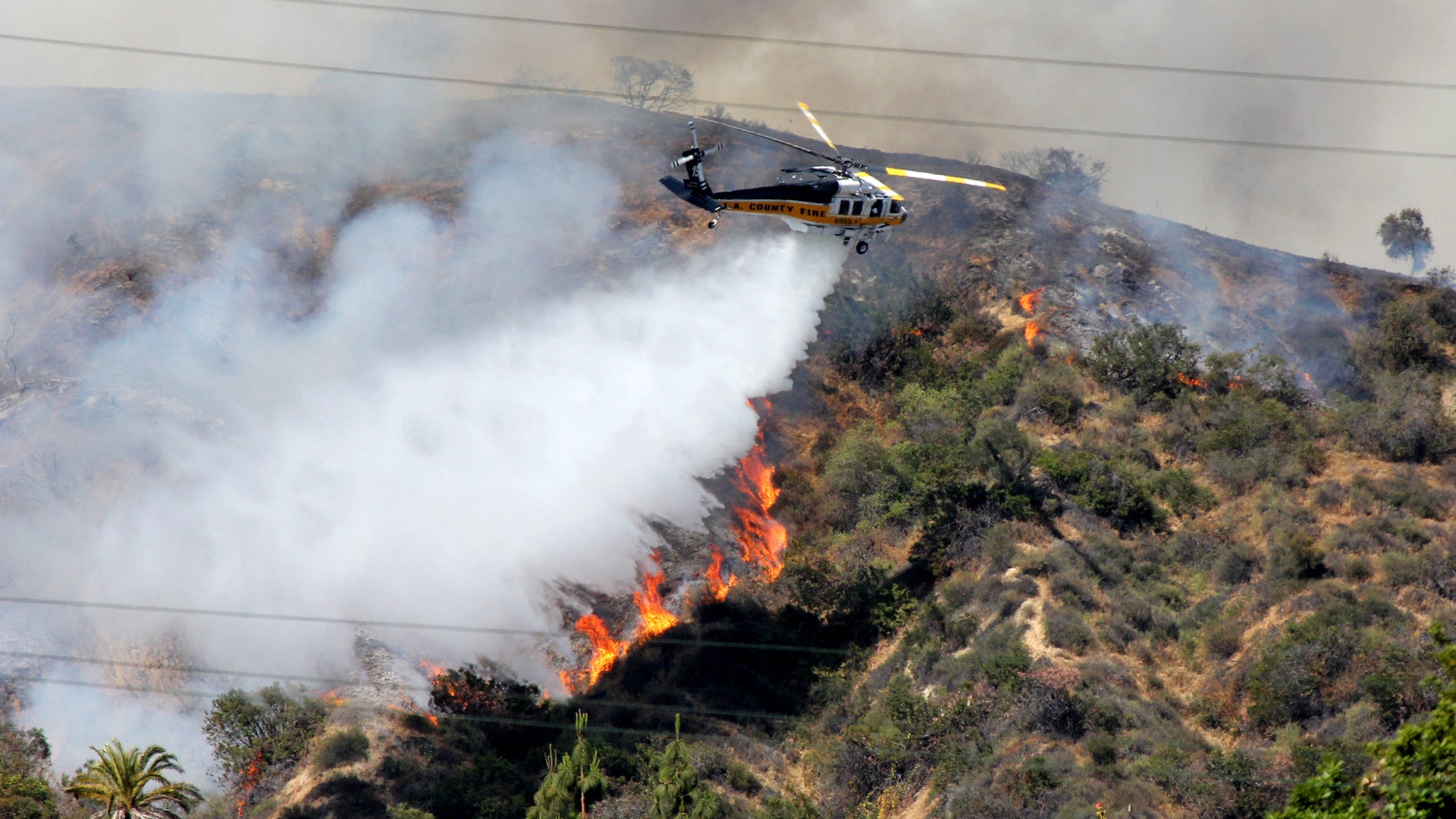 FILE - This Saturday April 20,2013 file photo shows a Los Angeles County Fire Department helicopter droping water on a fire burning on the foothills of the San Gabriel Mountains in Monrovia, Calif. Authorities say California is facing a dangerous wildfire season due to a dry winter that has left the normally green hills of spring parched and tinder-dry. (AP Photo/John Antczak,File)