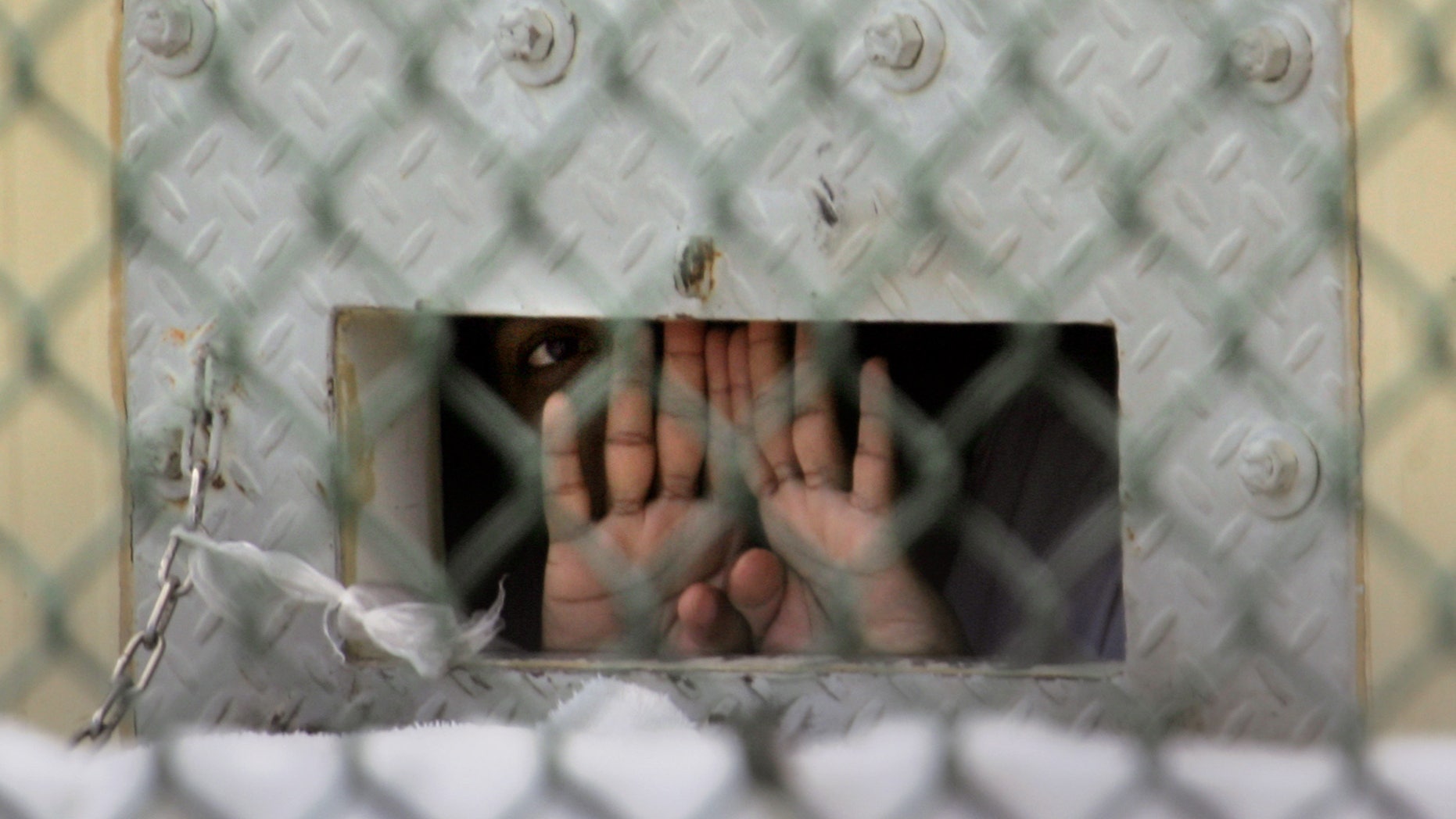 FILE - In this Dec. 4, 2006 file photo reviewed by a U.S. Dept of Defense official, a detainee shields his face as he peers out through the so-called "bean hole" which is used to pass food and other items into detainee cells, at Camp Delta detention center, Guantanamo Bay U.S. Naval Base, Cuba. Lt. Col. Samuel House said Friday, April 26, 2013 that 97 men are now on strike, up three from the day before. He says 19 of them are receiving liquid nutrients through a nasal tube to prevent dangerous weight loss. Another five are under observation at the hospital on the U.S. base in Cuba. The hunger strike began in February 2013, with prisoners protesting conditions and their indefinite confinement. The U.S. holds 166 prisoners at Guantanamo, most without charges. (AP Photo/Brennan Llinsley)
