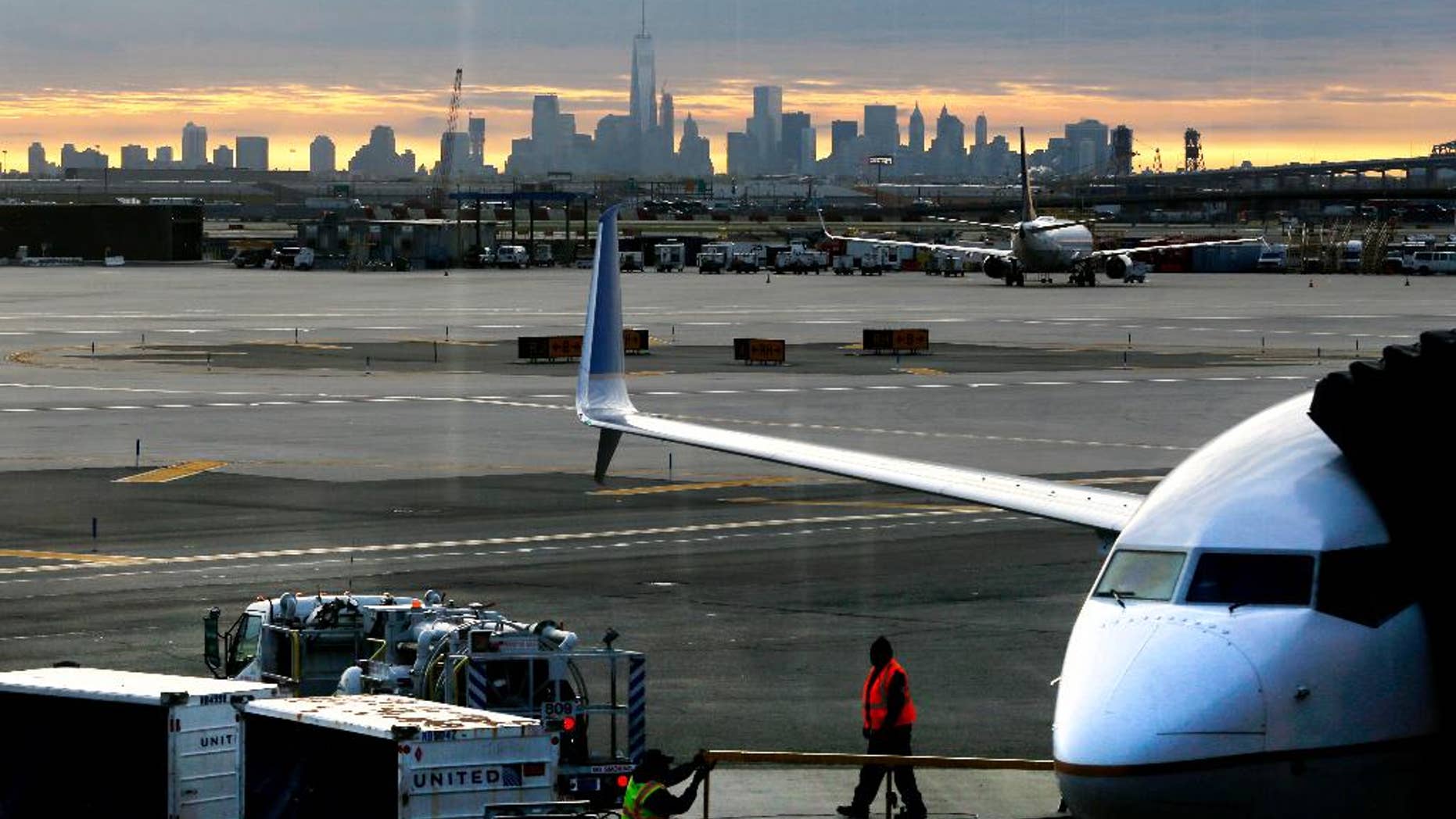 FILE - In a May 1, 2015 file photo, a United Airlines employee walks near a jet parked at Terminal C of Newark Liberty International Airport as the sun rises behind the New York City skyline, in Newark, N.J. The Federal Aviation Administration announced Friday, April 1, 2016, that it is easing limits on the number of hourly flights at Newark Liberty International Airport, and the airport’s operator said that should lead to greater competition and lower fares.(AP Photo/Julio Cortez, File)