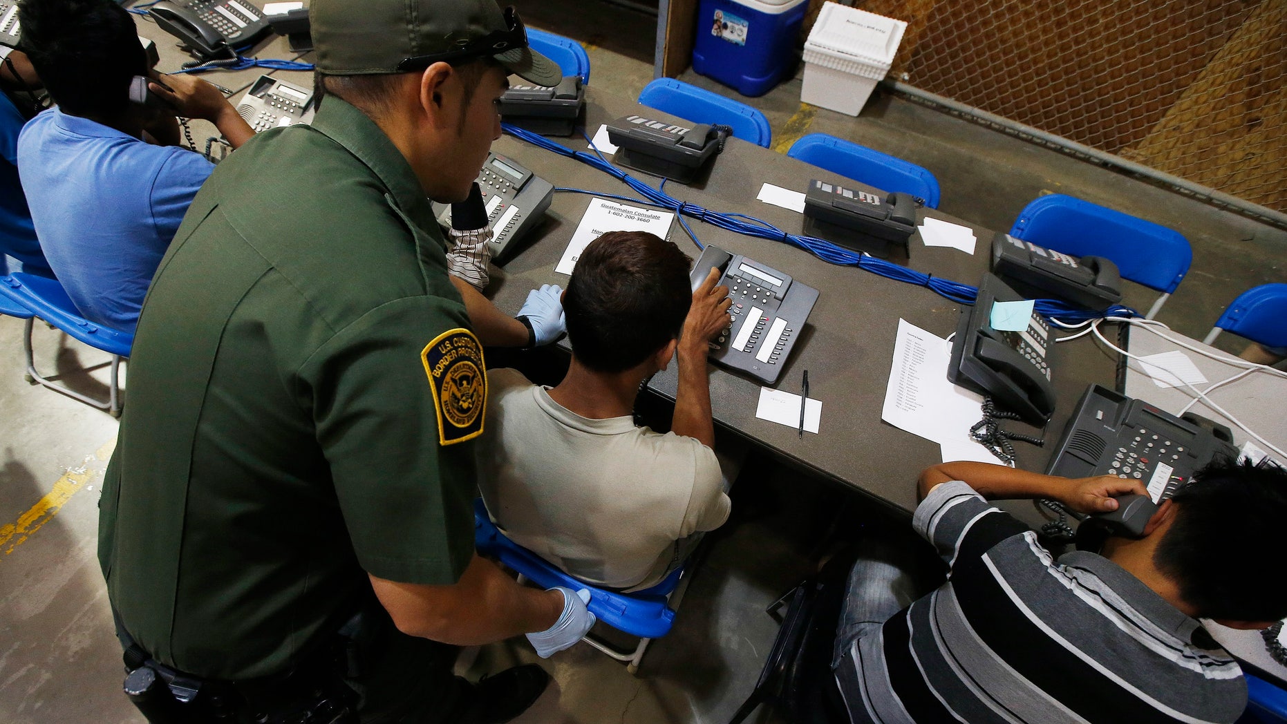 A U.S. Customs and Border Protection officer helps out a few boys who are trying to make phone calls as they are joined by hundreds of mostly Central American immigrant children that are being processed and held at the U.S. Customs and Border Protection Nogales Placement Center on Wednesday, June 18, 2014, in Nogales, Ariz. CPB provided media tours Wednesday of two locations in Brownsville, Texas, and Nogales, that have been central to processing the more than 47,000 unaccompanied children who have entered the country illegally since Oct. 1. (AP Photo/Ross D. Franklin, Pool)