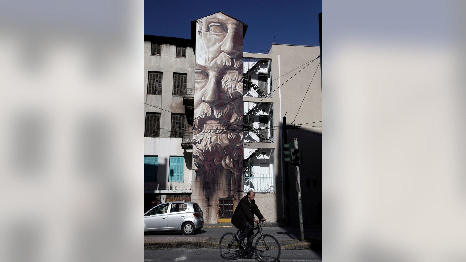 A cyclists passes a mural named 'System of Fraud' in an inner city area of Athens, on Wednesday, Jan. 29, 2014. The painting by the Greek street artist known as iNO features the face of ancient Greek lawmaker Solon. iNO is one of Greece's best known street artists, with work in public areas in Berlin and Miami. Greek artists have made use of disused warehouse and building facades to display their artwork, often related to the country's acute financial crisis. (AP Photo/Dimitri Messinis)