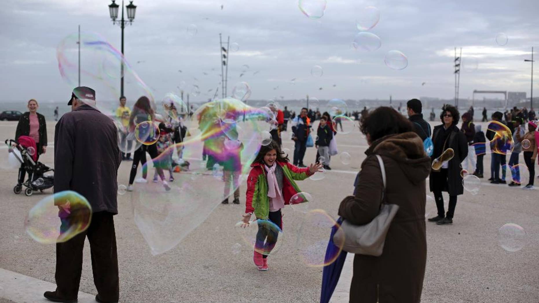 A child laughs as she tries to catch soap bubbles created by a street artist, in Lisbon's Comercio square, Tuesday, Jan. 3 2017. (AP Photo/Armando Franca)