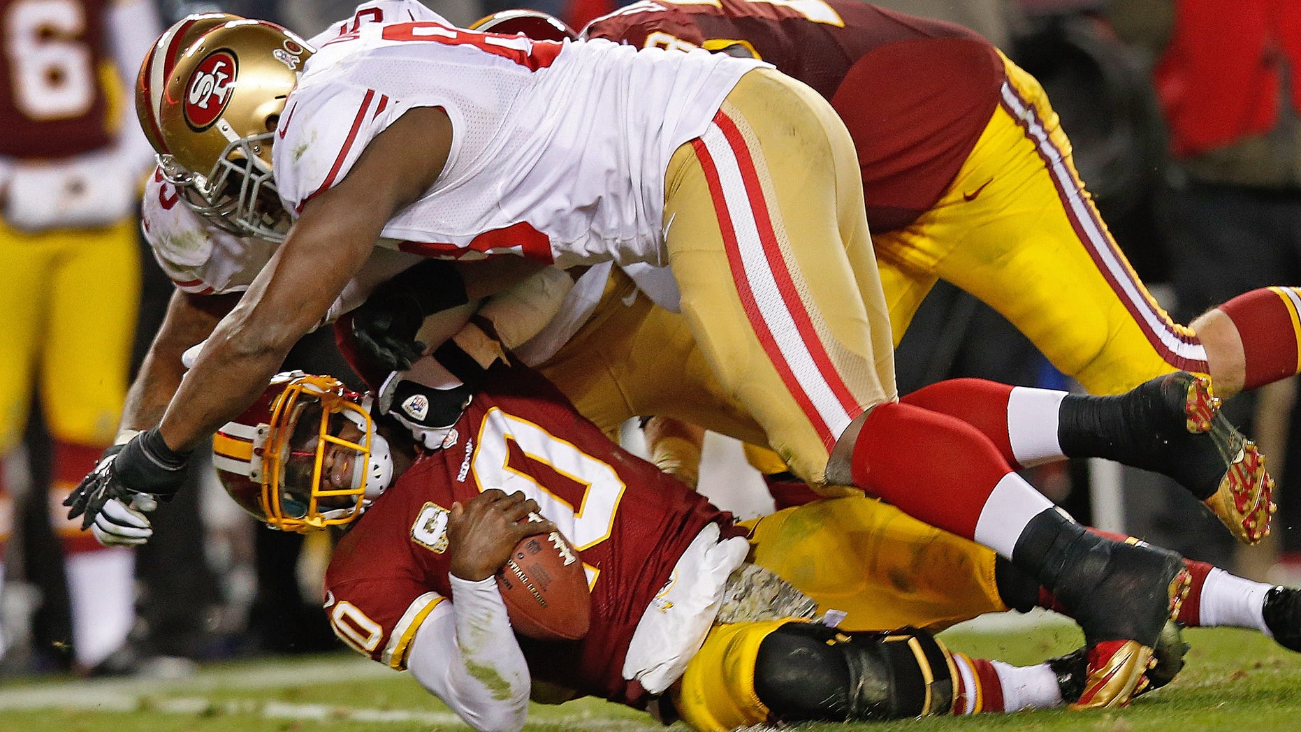 Washington Redskins quarterback Robert Griffin III is knocked to the turf by San Francisco 49ers tight end Demarcus Dobbs, front, and another defender during the second half of an NFL football game in Landover, Md., Monday, Nov. 25, 2013. The 49ers deafeted the Redskins 27-6. (AP Photo/Alex Brandon)