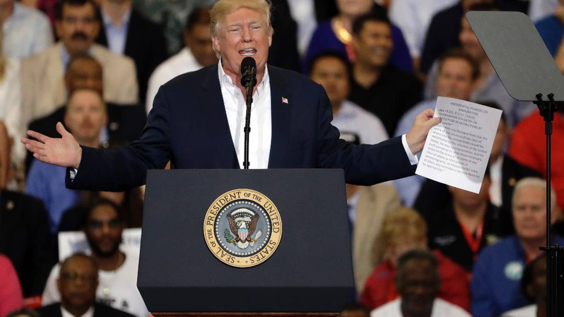 President Donald Trump gestures as he holds up a piece of paper on the presidential powers on immigration during a campaign rally Saturday, Feb. 18, 2017, at Orlando-Melbourne International Airport, in Melbourne, Fla. (AP Photo/Chris O'Meara)