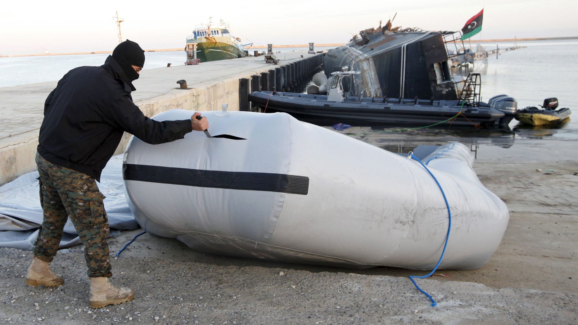 A member of the Libyan coast guard uses a knife to tear a dinghy used by migrants trying to escape to Europe last year.